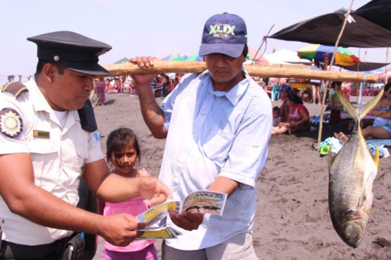 Agente Policial entrega a un vendedor de pescado guía de prevención para Semana Santa.
