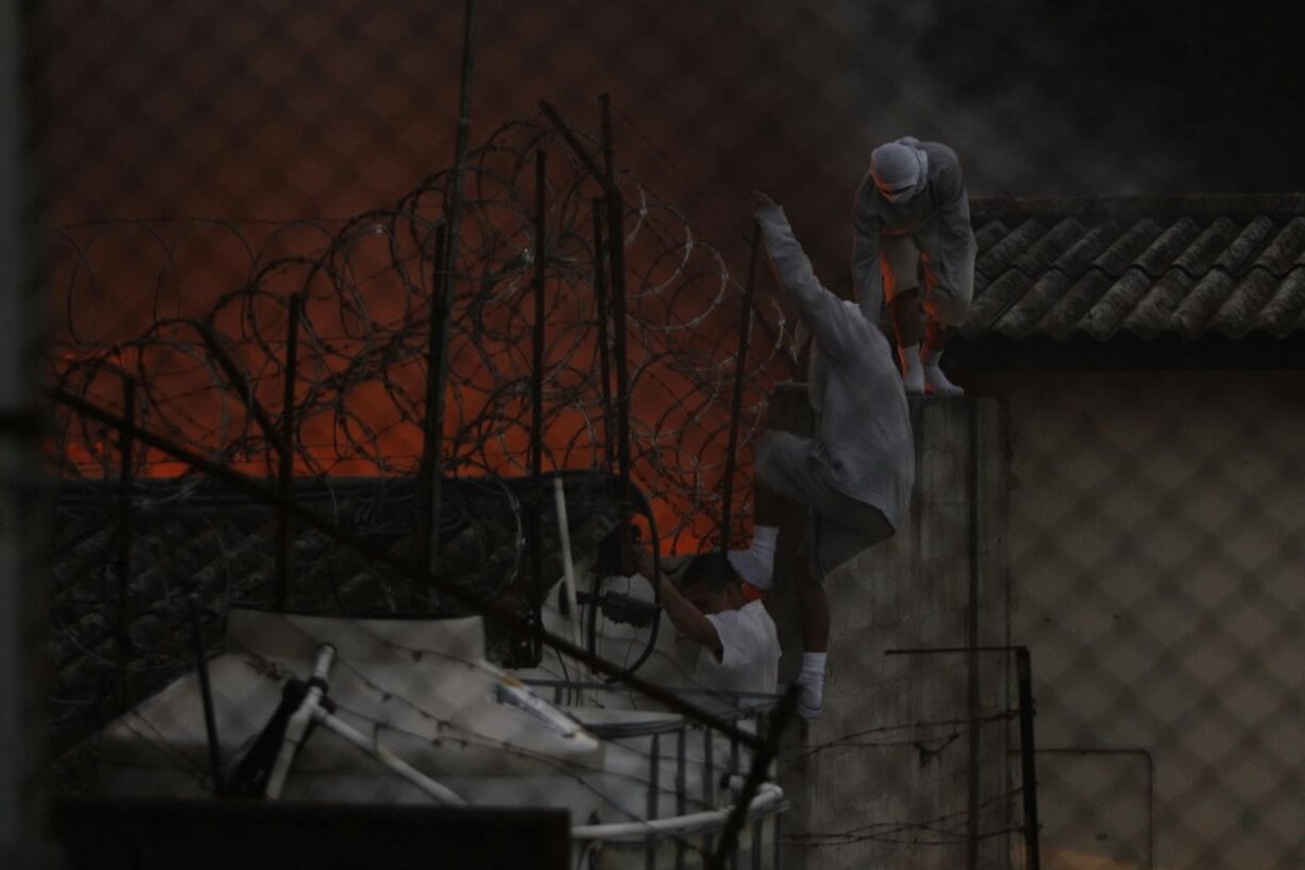 Internos caminan por el techo de uno de los ambientes. Al fondo, un incendio. (Foto Prensa Libre: Paulo Raquec)