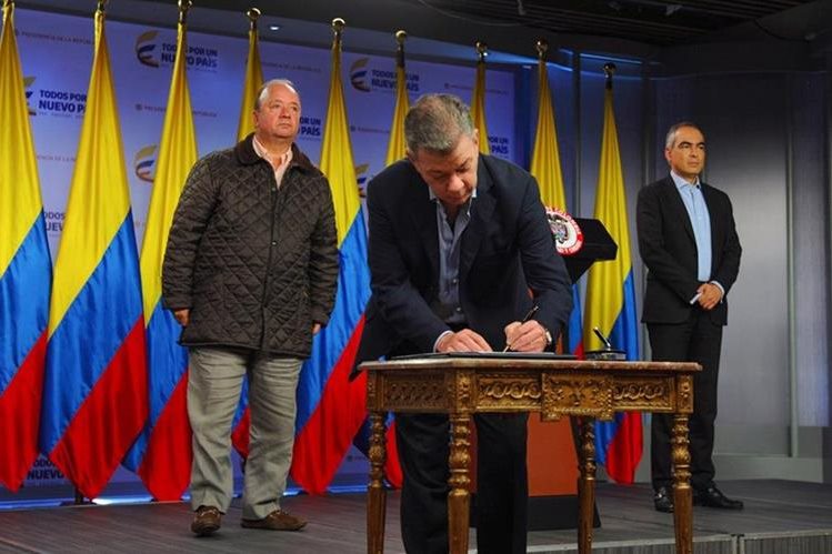 El presidente colombiano Juan Manuel Santos (C), acompañado por el ministro de Defensa Luis Carlos Villegas (i) y el comisionado por la Paz Rodrigo Rivera, firmando el alto el fuego con la guerrilla del ELN. (AFP).