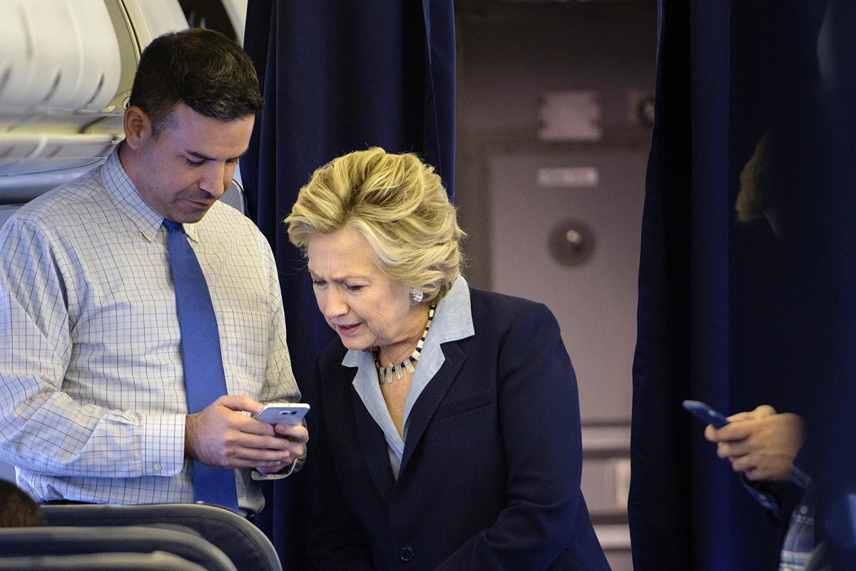 La candidata presidencial Hillary Clinton oberva el celular de su jefe de campaña Brian Fallon en el avión que la transporte. (Foto Prensa Libre: AFP).