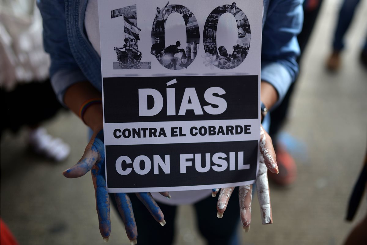 Un estudiante sostiene un letrero que dice "100 días contra el cobarde con rifle" durante una vigilia para conmemorar los 100 días de protestas contra Ortega. (AFP)