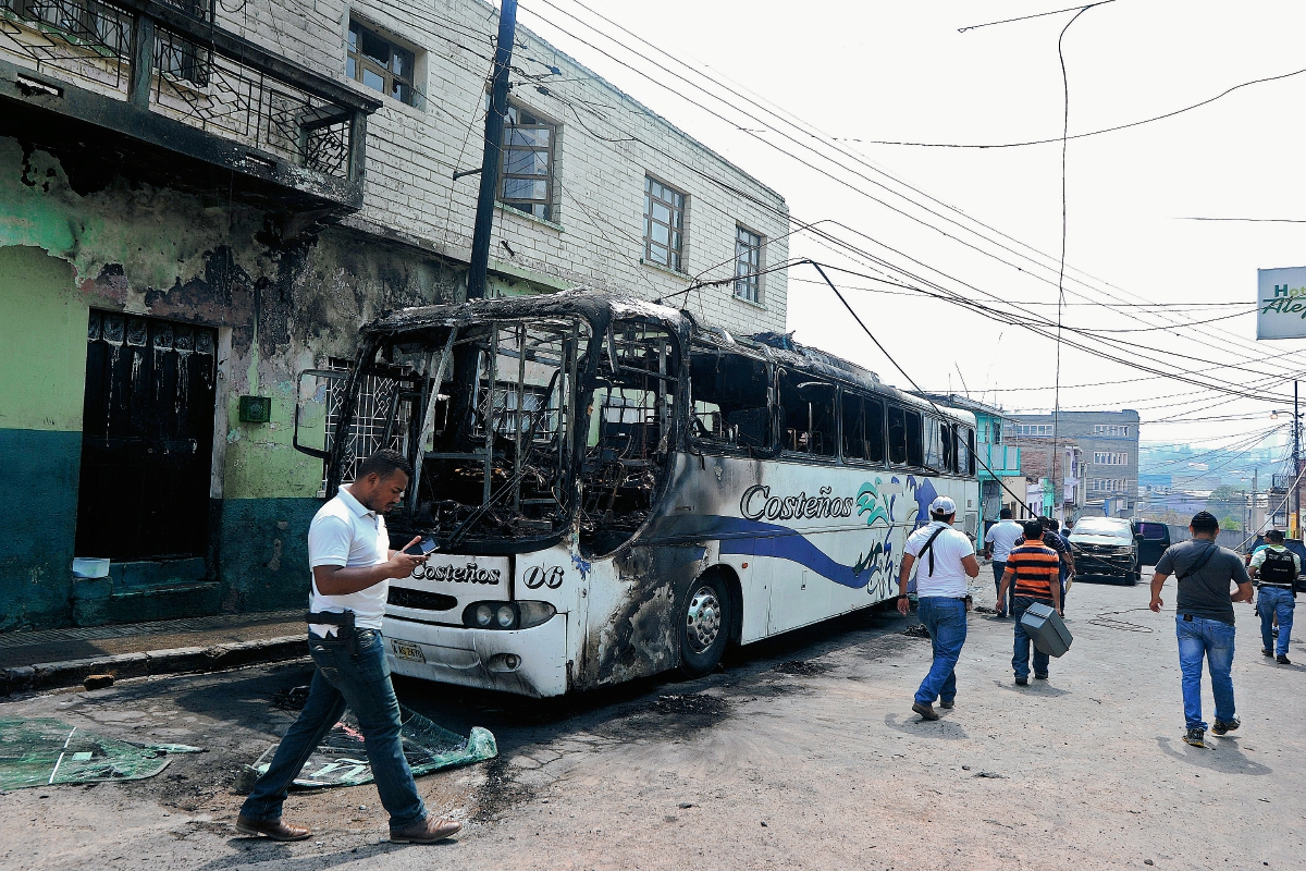 Investigadores observan el bus que fue incendiado por pandilleros el jueves último porque no pagaron a tiempo el “impuesto de guerra”, que les exigen para circular en Tegucigalpa. (Foto Prensa Libre: AFP).