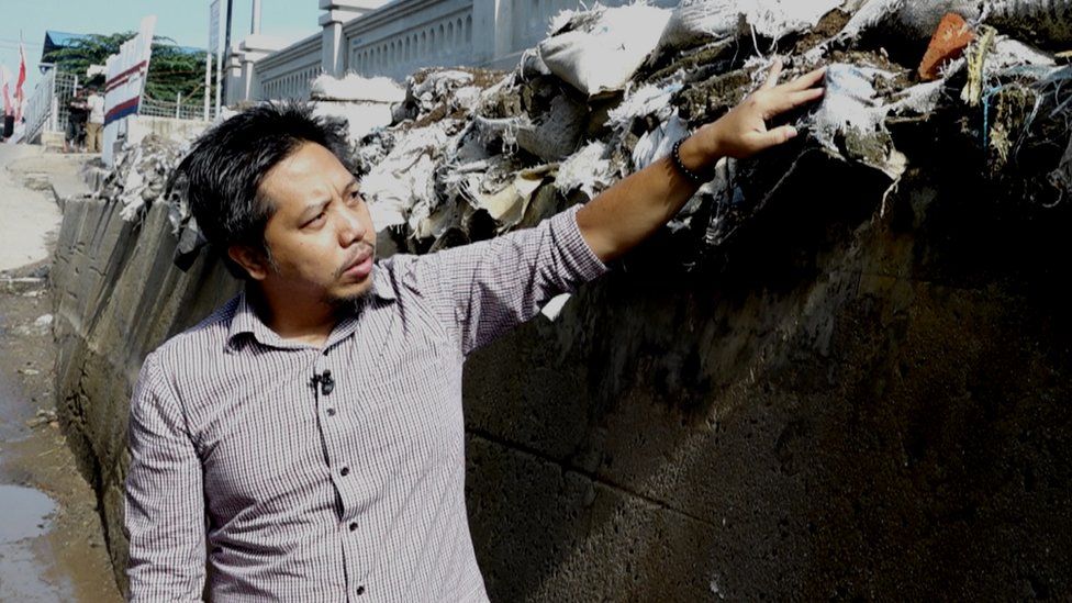 Heri Andreas señala un dique construido para evitar que el agua del mar inunde las casas cuando llueve.