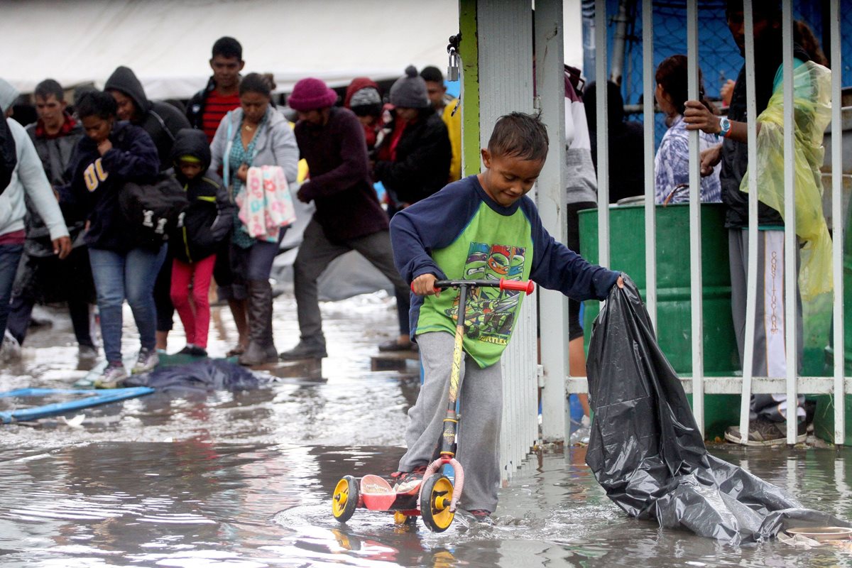 Un niño juega bajo la lluvia luego de que el albergue en el que se concentraban los integrantes de la caravana migrante se inundara. La Unicef expresa preocupación por estos menores. (Foto Prensa Libre: EFE