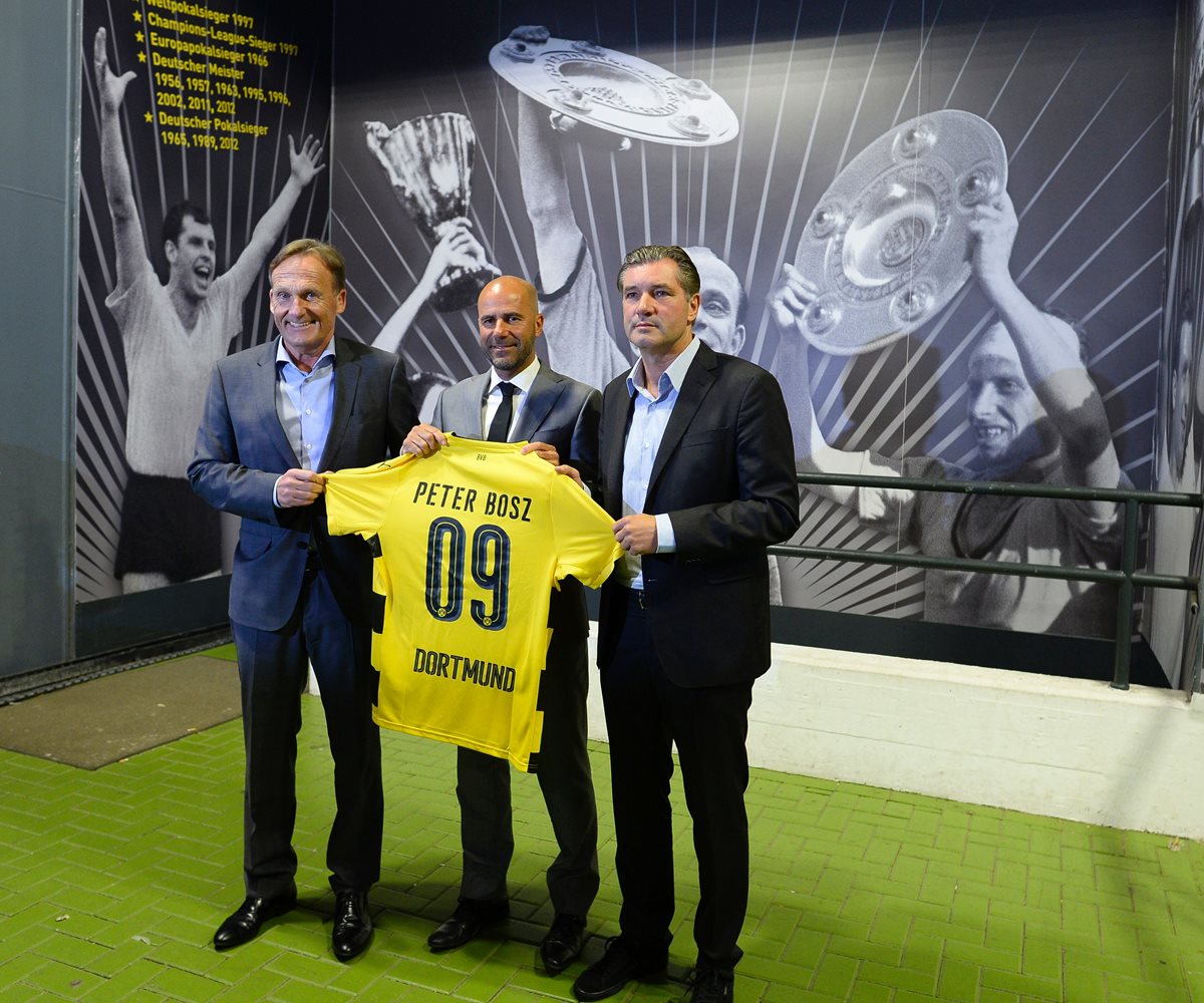 Peter Bosz posa con la camisola del Borussia Dortmundo junto a los directivos del club Hans-Joachim Watzke y Michael Zorc. (Foto prensa Libre: AFP)