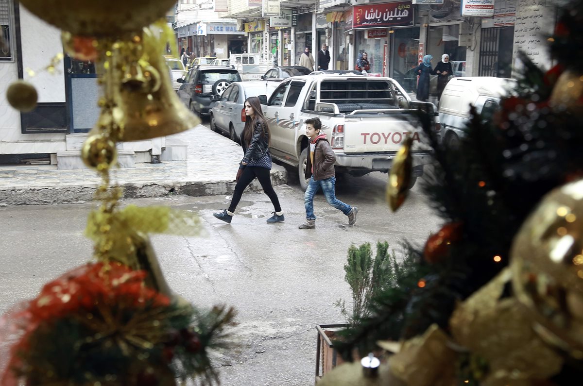 Dos jóvenes sirios caminan en una de las calles del barrio cristiano de Qamishli, donde la celebración de la Navidad ha quedado relegada. (Foto Prensa Libre: AFP).