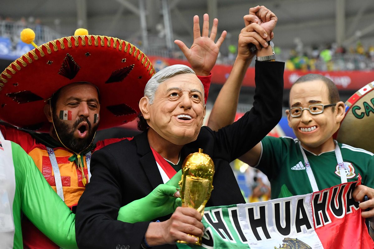 Un fanático de México porta una máscara que representa a Andrés Manuel López Obrador, aplaude con otros simpatizantes antes del partido de futbol entre Brasil y México. (AFP).
