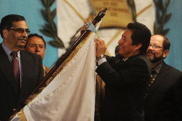 El ministro de Cultura y Deportes, Carlos Batzín, coloca la insignia en la bandera del Medio Maratón de Cobán, sostenida por Juan de Dios Reyes. (Foto Prensa Libre: Romeo Ríos)