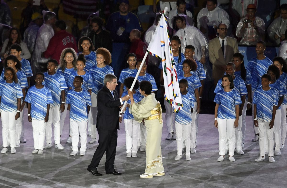 Thomas Bach (c), presidente del Comité Olímpico Internacional (COI), le entrega la bandera olímpica a la gobernadora de Tokio, Yuriko Koike (Foto Prensa Libre: AFP)