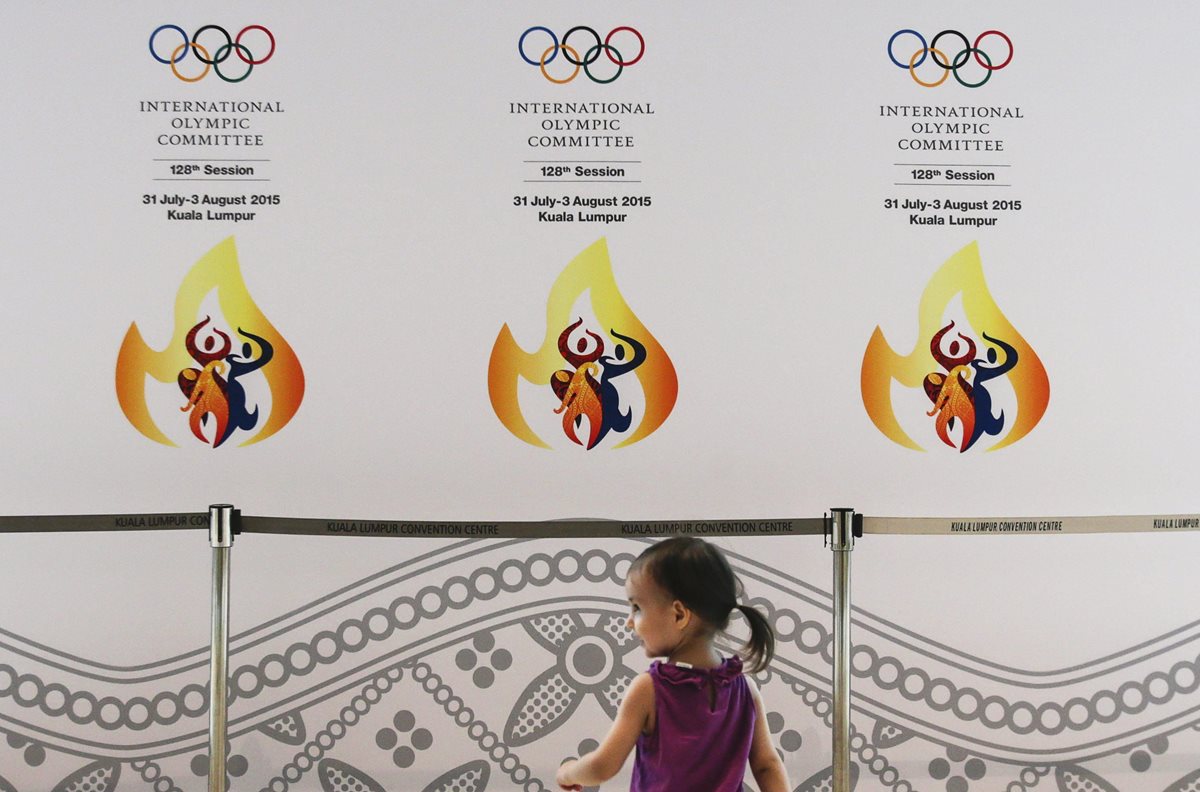 Una niña sonríe delante de un cartel anunciador de la reunión del COI) en Kuala Lumpur. (Foto Prensa Libre: EFE)