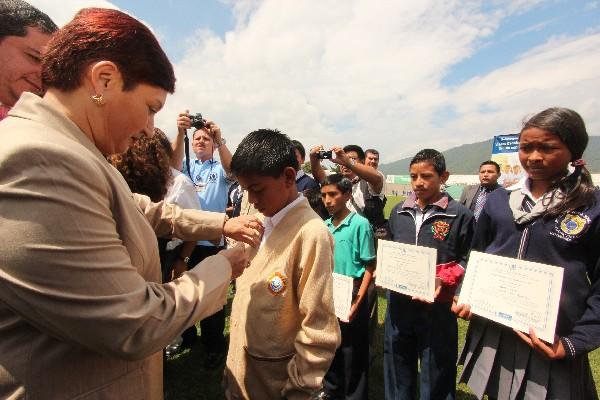 la presidenta de la CSJ,  Thelma Aldana, coloca un pin al estudiante José Antonio Reguán Apén.