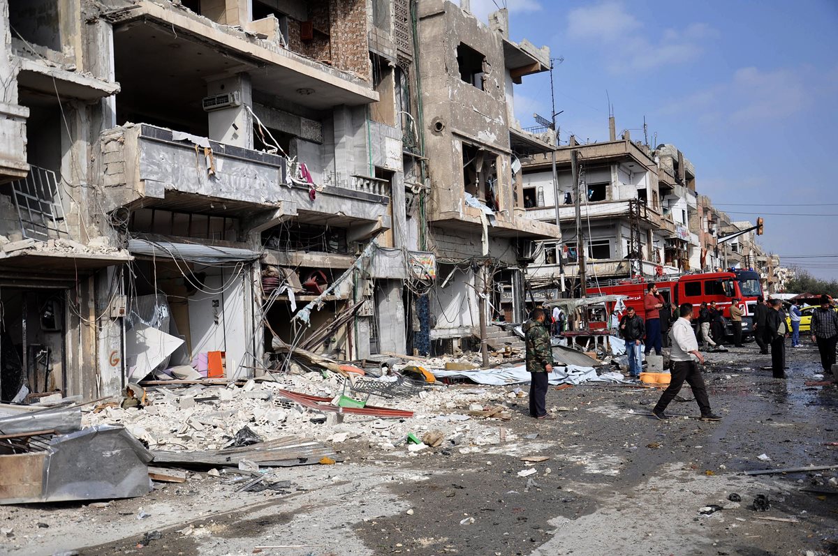 Policías y ciudadanos sirios inspeccionan el sitio de un ataque con bomba doble en la ciudad de Homs, Siria, el 21 de febrero del 2015. (Foto Prensa Libre: EFE).