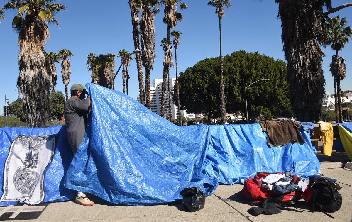 En esta fotografía tomada en febrero de 2016 un hombre permanece en una champa; al fondo los suntuosos edificios angelinos. (Foto Prensa Libre: AFP).