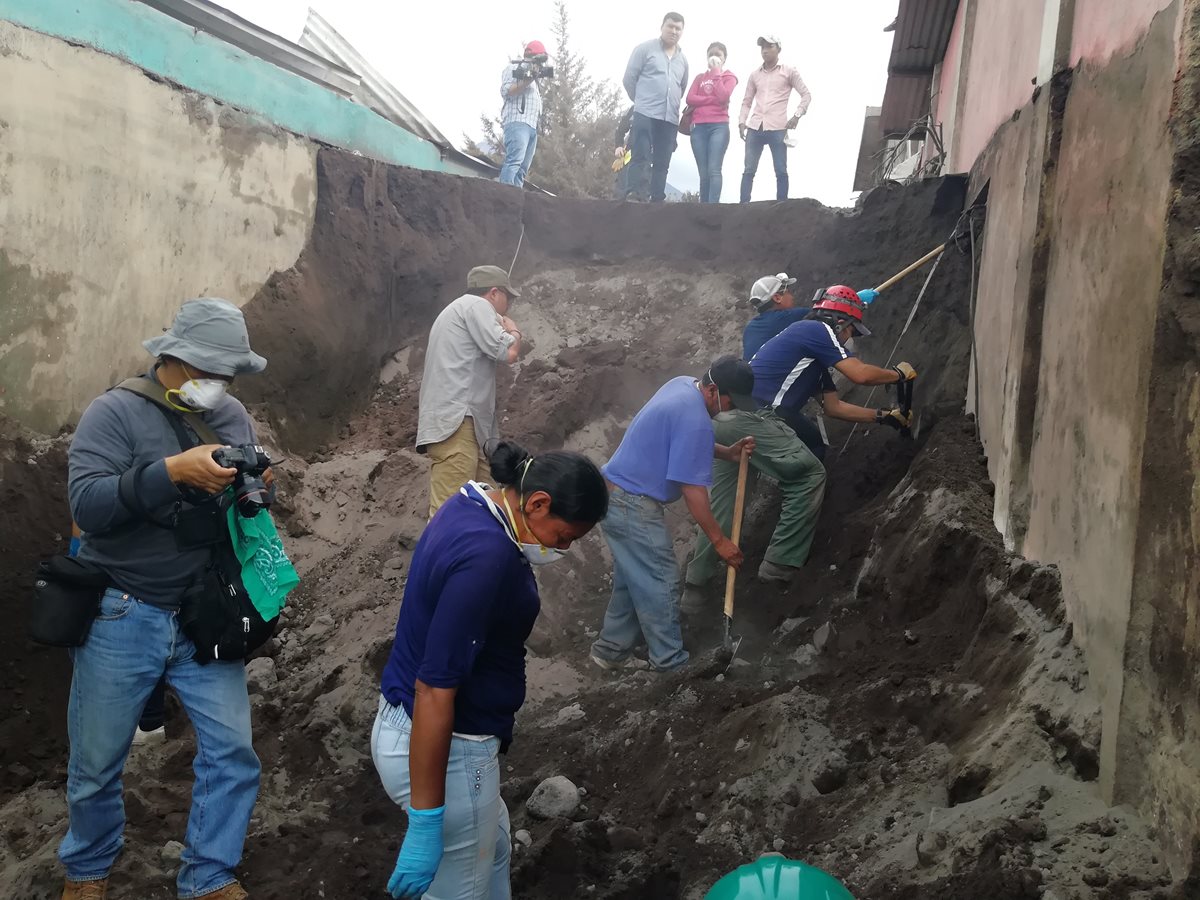 Damnificados y socorristas guían al operario de una máquina retroexcavadora que remueve arena volcánica en el callejón principal de San Miguel Los Lotes, El Rodeo, Escuintla. (Foto Prensa Libre: Carlos Paredes)