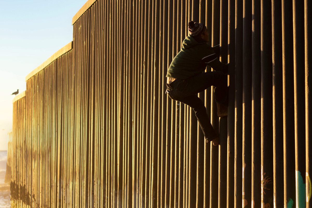 Un migrante hondureño escala el muro fronterizo entre México y Estados Unidos. (Foto Prensa Libre: AFP)