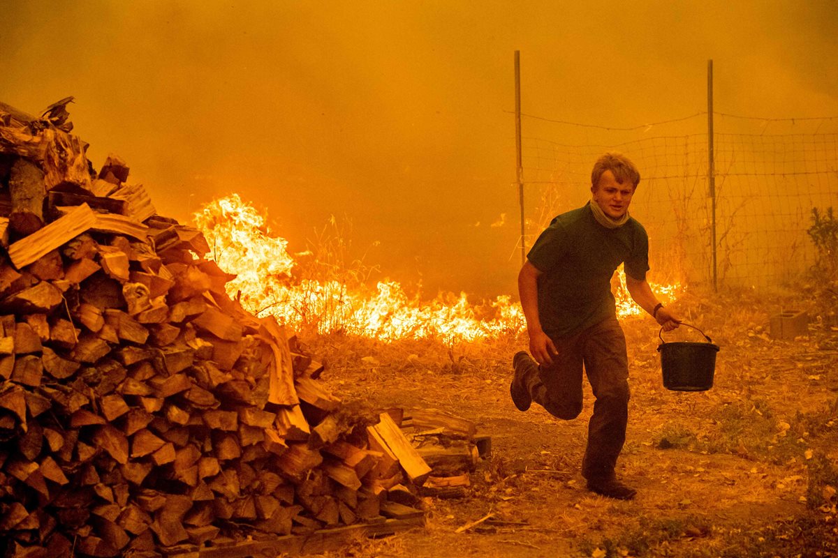 Alex Schenck lleva un balde de agua mientras lucha para salvar su casa en New Long Valley Rd cerca de Clearlake Oaks, California. (AFP)