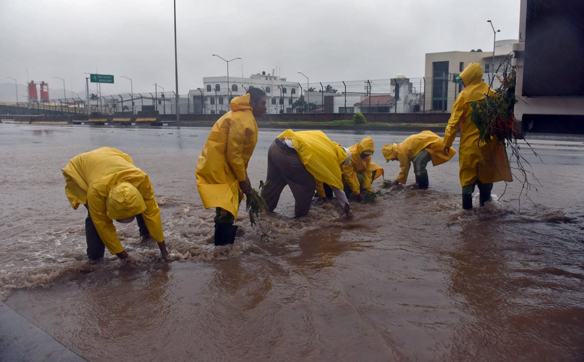 Trabajadores municipales despejan tragantes en una calle en Manzanillo, Colima, México.(Foto Prensa Libre: AFP).