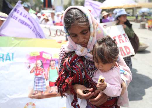 Doña María comparte un banano con Marcela, su hija de un año, mientras participan en la marcha. (Foto Prensa Libre: Óscar Rivas)