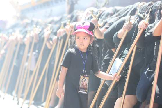 Una niña porta un gorro de una figura animada mientras acompaña a su madre en la procesión. 