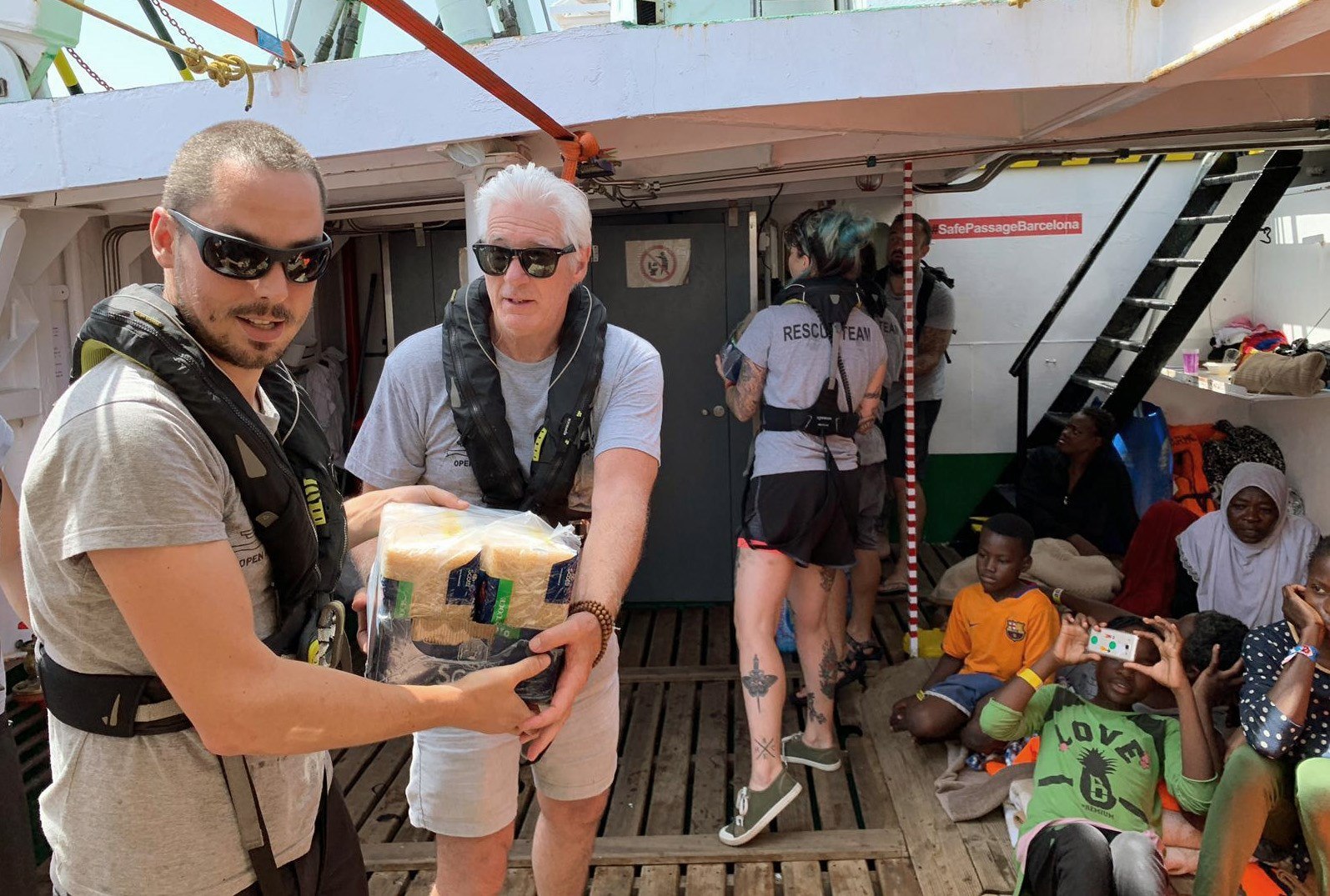 El actor estadounidense Richard Gere -derecha- entrega víveres en el barco que alberga a migrantes. (Foto Prensa Libre: EFE). 