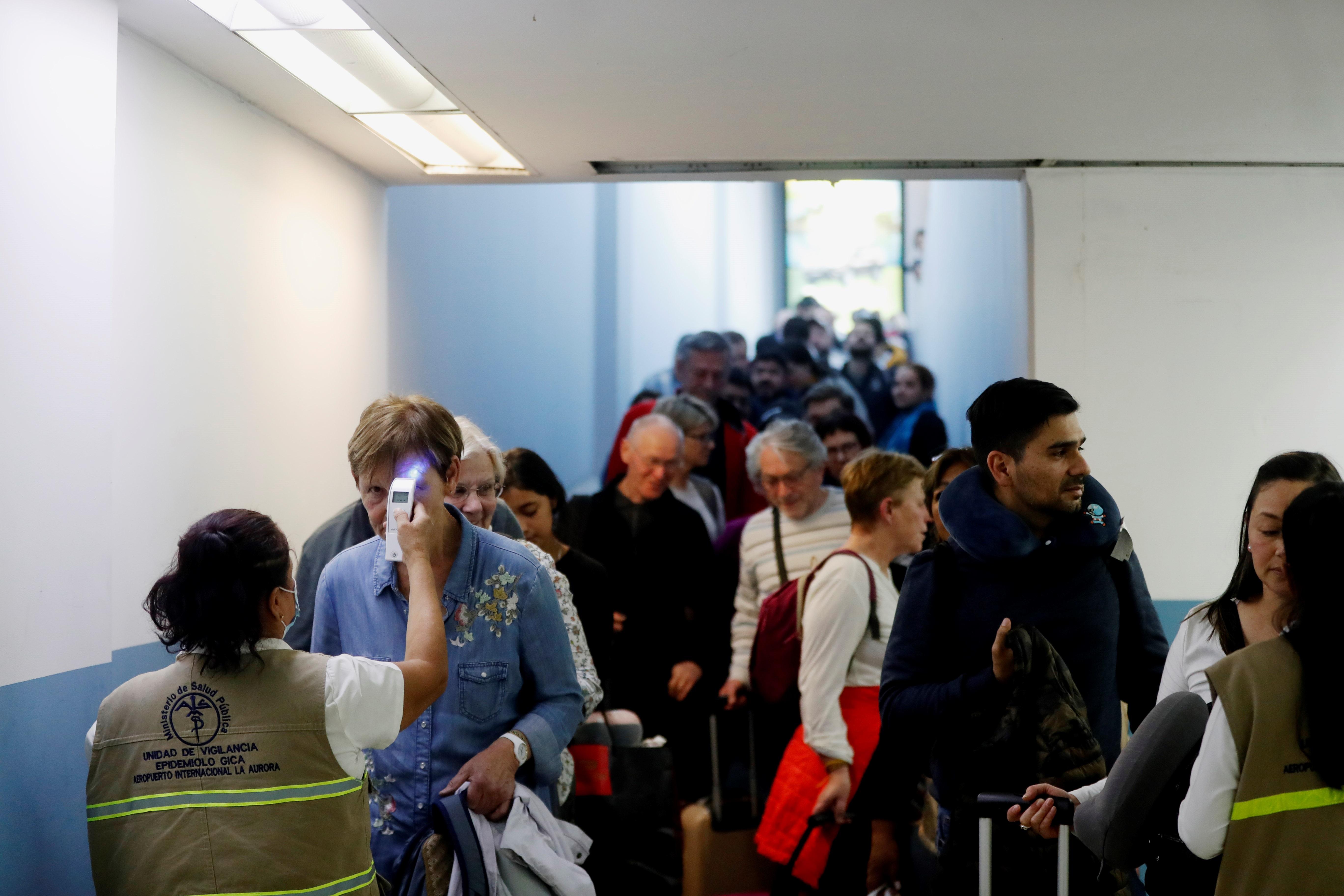 Trabajadores del Ministerio de Salud revisan la temperatura de pasajeros provenientes de un vuelo de Europa. (Foto Prensa Libre: EFE)