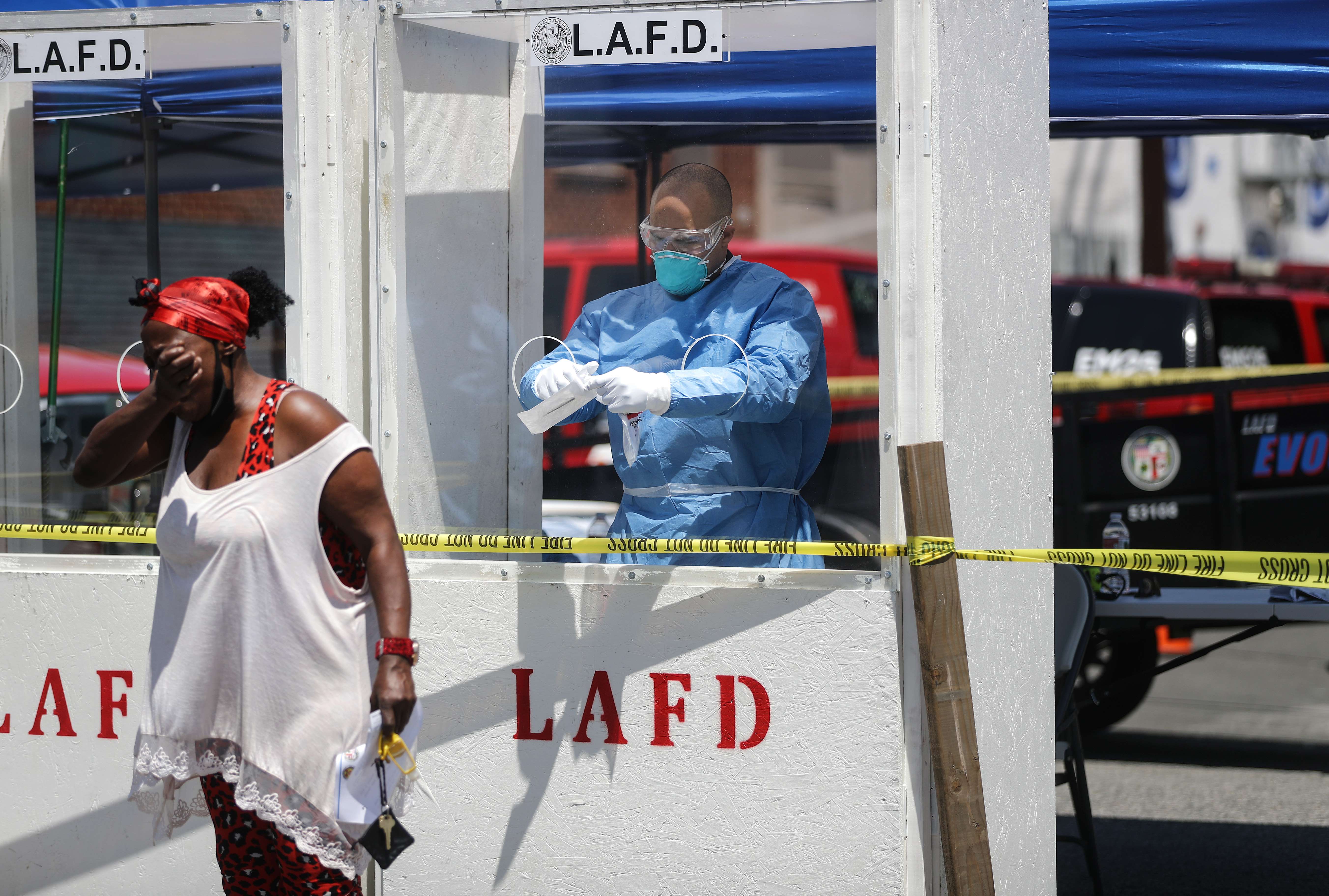 Un miembro del Departamento de Bomberos de Los Ángeles que usa equipo de protección personal (PPE) en Skid Row, en medio de la pandemia de coronavirus, le pide a una mujer que tosa en su brazo como parte de la prueba de covid-19, el 21 de abril de 2020 en Los Ángeles, California. (Foto Prensa Libre: AFP)
