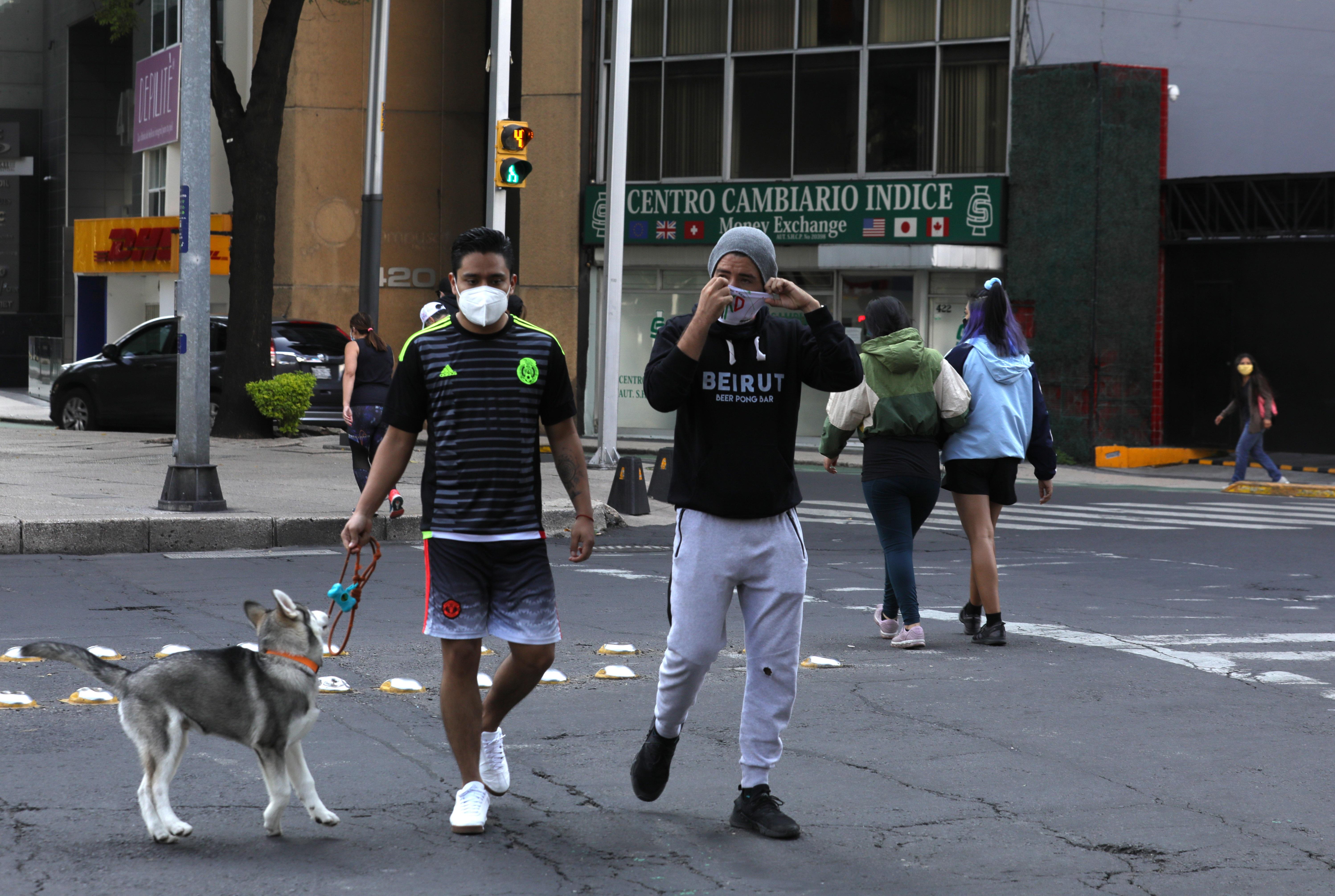 Dos hombres usan mascarilla, mientras pasean con su perro en una calle de la ciudad de México. Foto Prensa Libre: EFE