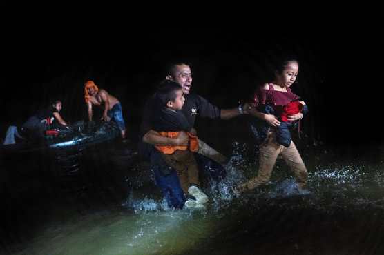 Un padre migrante agarra a sus hijos mientras camina hacia la orilla del río Bravo en la frontera entre Estados Unidos y México en Roma, Texas. (Foto Prensa Libre: AFP)