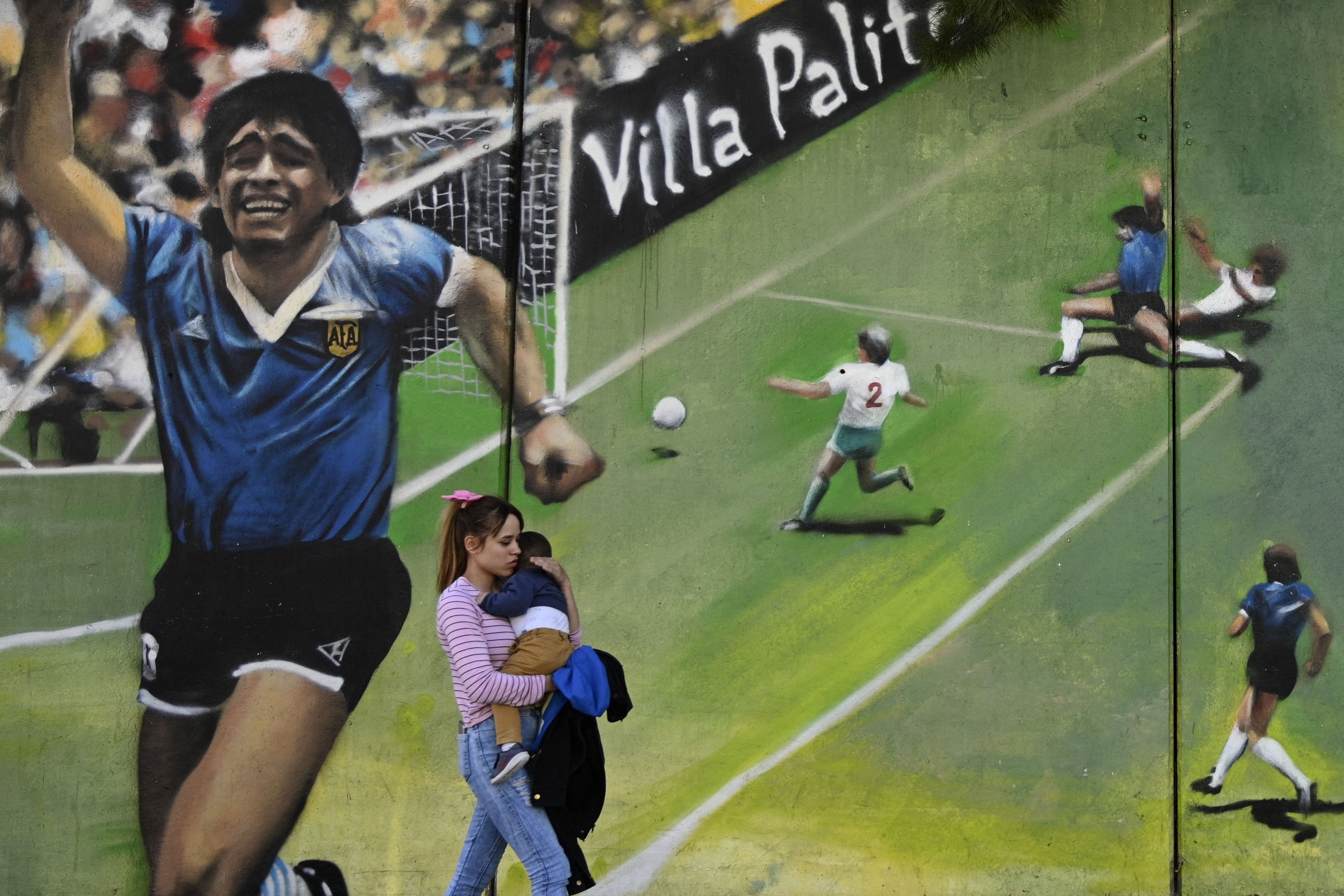 En esta foto, tomada el 30 de octubre de 2020, una mujer pasa por un mural del artista "Uasen" que riden tributo al gol del siglo de Diego Maradona. Foto Prensa Libre: AFP.