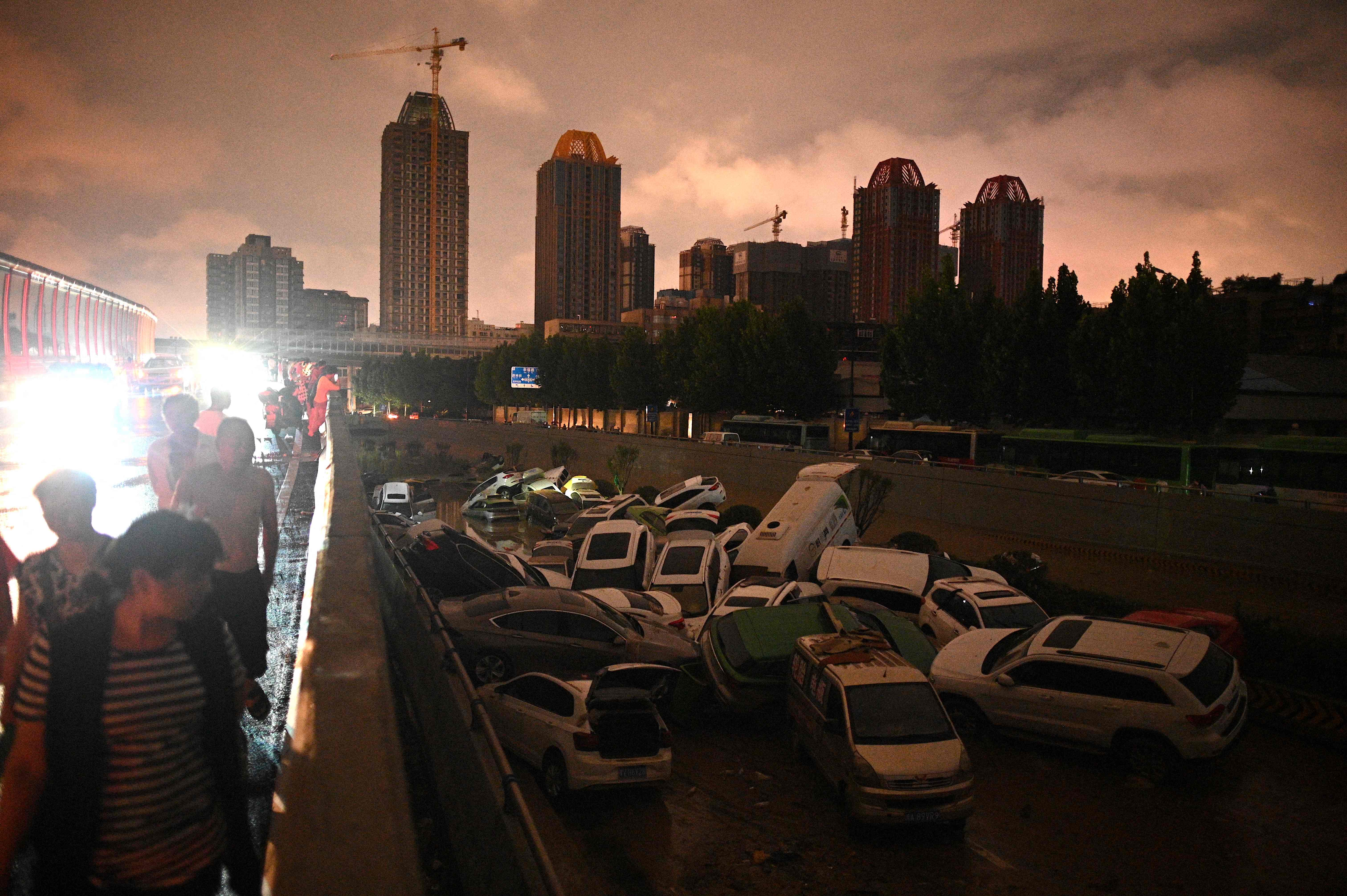 La gente mira los autos apilados unos sobre otros en la entrada de un túnel luego de una fuerte lluvia en Zhengzhou, en la provincia china de Henan (Foto: Prensa Libre. AFP).