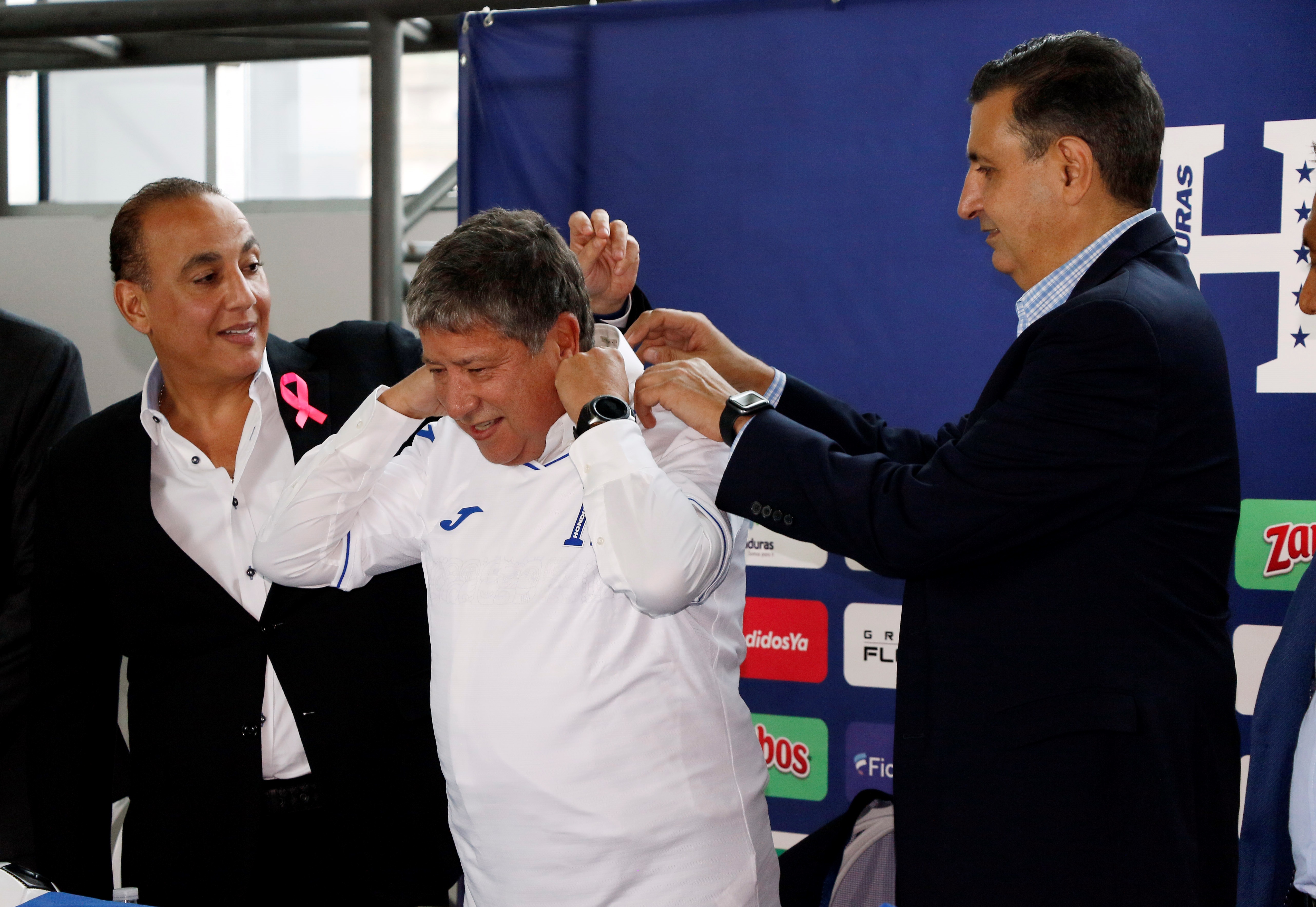 El primer vicepresidente del Comité Ejecutivo de la Fenafuth, Javier Átala (i), el presidente de Fenafuth, Jorge Salomónes (d), ayudan al colombiano Hernán Darío "Bolillo" Gómez a vestirse con la camisa de la selección de Honduras. (Foto Prensa Libre: EFE).
