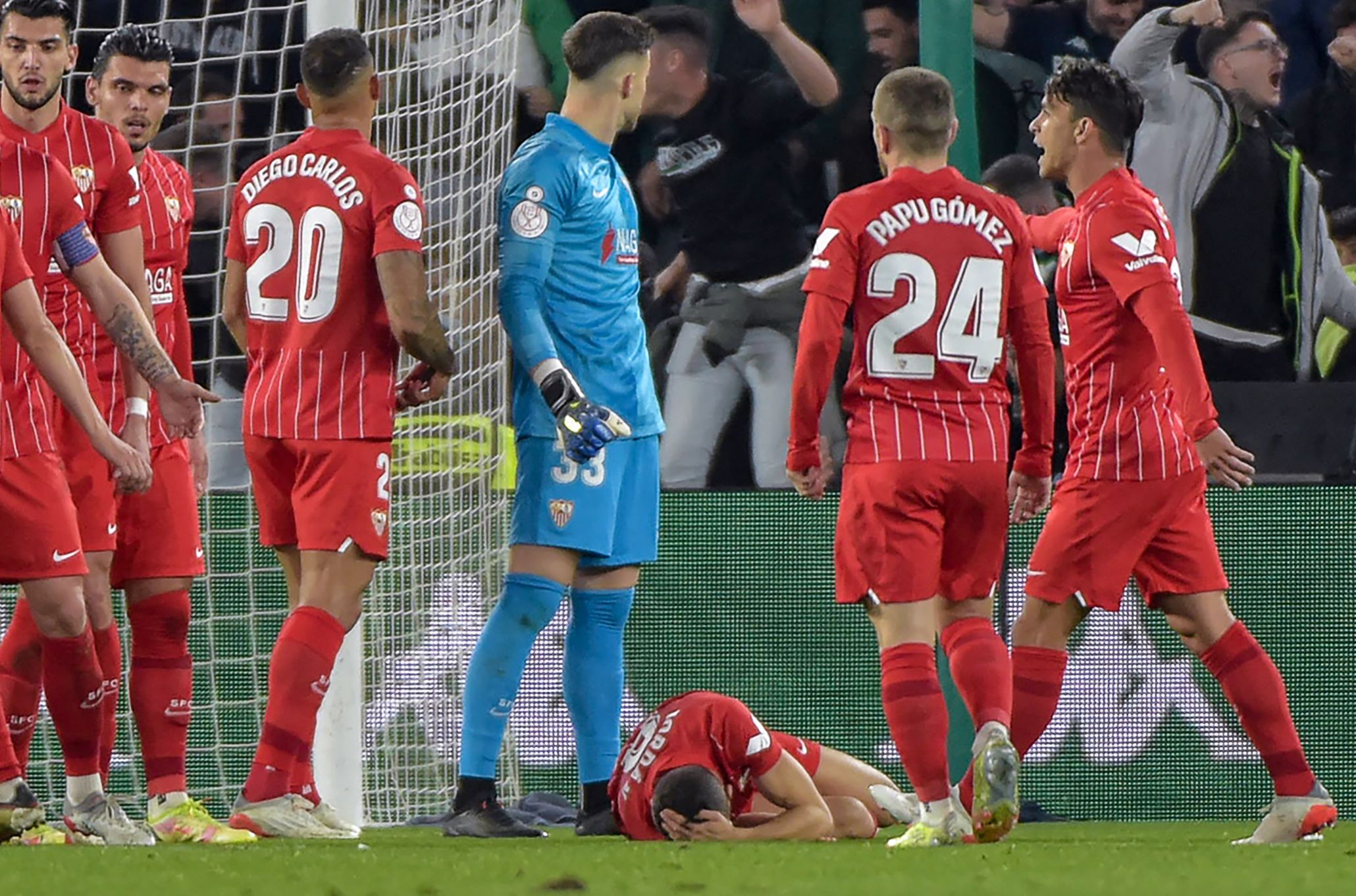 El jugador del Sevilla Joan Jordán Moreno (centro) recostado en la cancha luego de ser alcanzado por un objeto de plástico lanzado desde la tribuna de los aficionados al Real Betis. (Foto Prensa Libre: AFP)