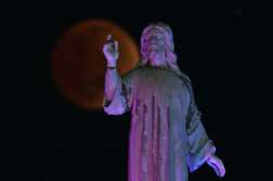 The blood moon is seen during a total lunar eclipse past the Savior of the World monument in Salvador del Mundo Square, in San Salvador on November 8, 2022. (Photo by Marvin RECINOS / AFP)