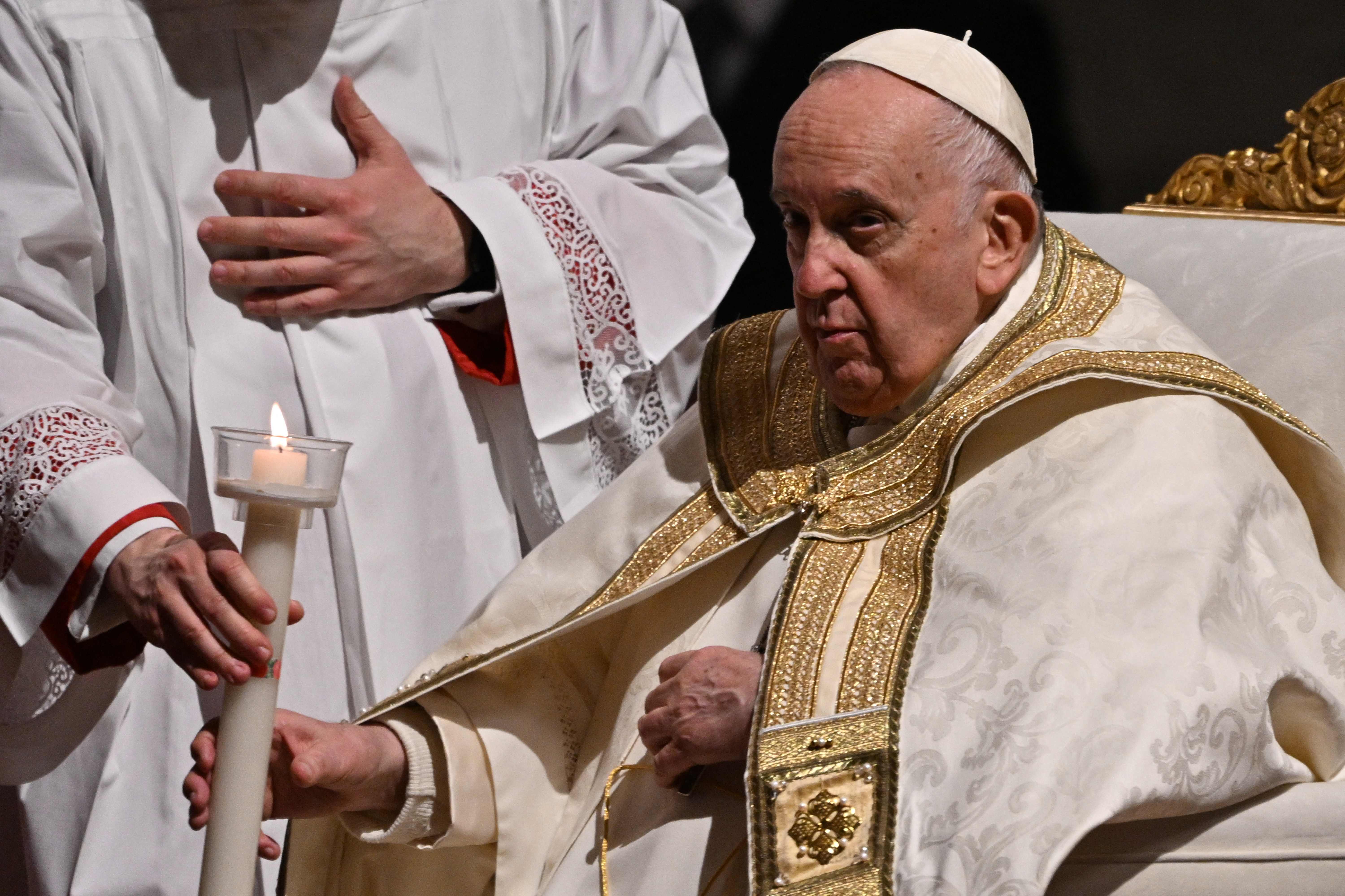 Pope Francis, remaining seated, holds his candle lit from the Easter Candle, during the opening of the Easter Vigil mass on April 8, 2023 at St. Peter's basilica in The Vatican, as part of celebrations of the Holy Week. (Photo by Andreas SOLARO / AFP)