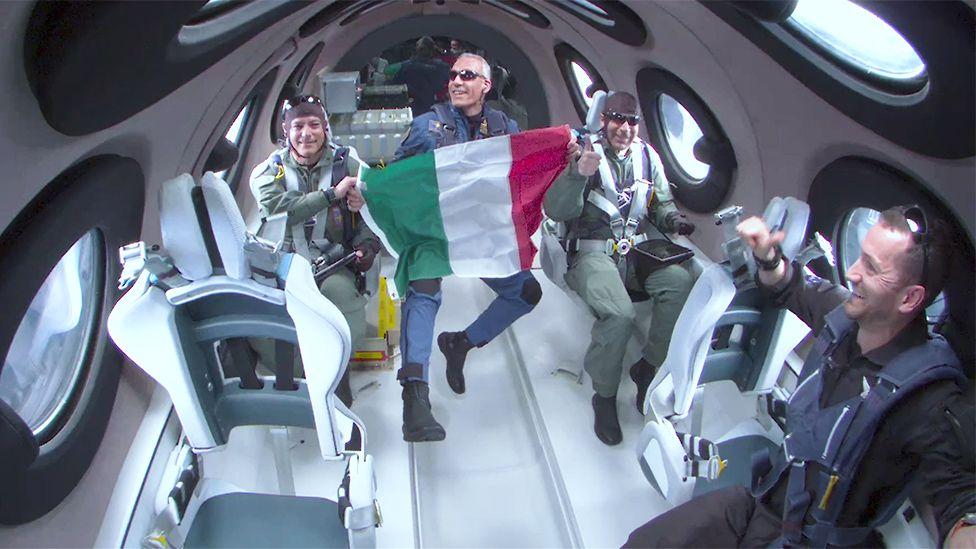 Los miembros italianos del equipo a bordo de la nave Unity sostienen la bandera de su país en el espacio.