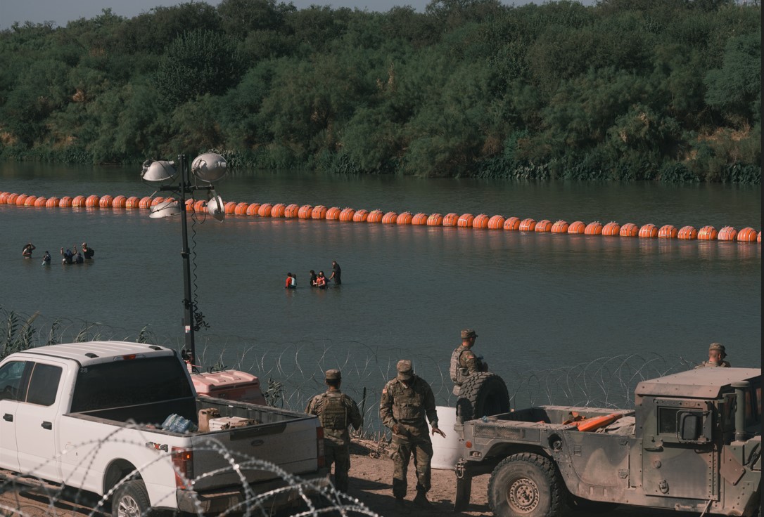 Migrantes en el río Bravo junto a una cadena de boyas destinadas a disuadir que crucen el río, en Eagle Pass, Texas, el 8 de agosto de 2023. (Jordan Vonderhaar/The New York Times)