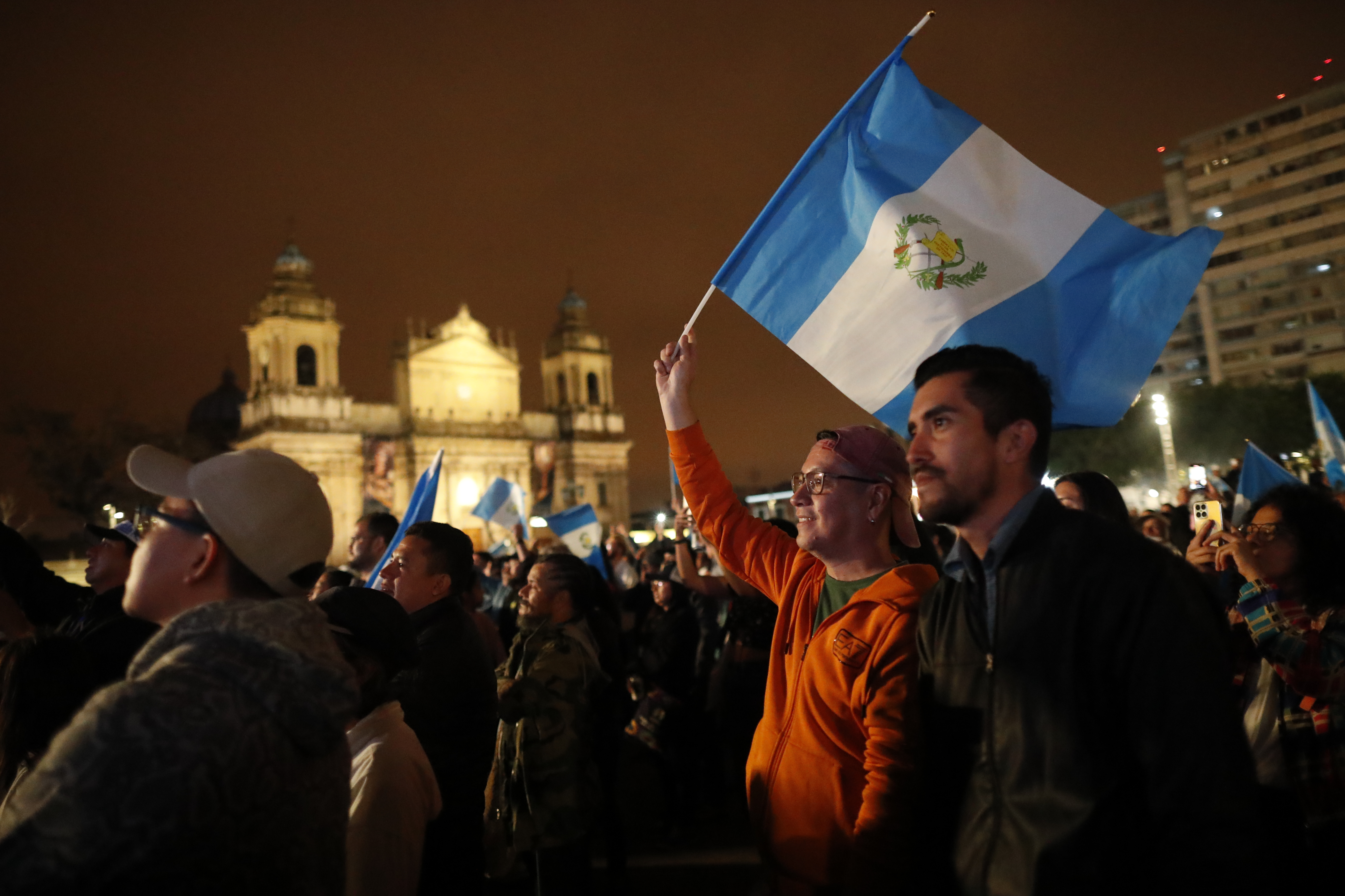 AME9901. CIUDAD DE GUATEMALA (GUATEMALA), 15/01/2024.- Personas reaccionan a la transmisión de la posesión nuevo presidente de Guatemala, Bernardo Arévalo hoy, en Plaza de la Constitución, en Ciudad de Guatemala (Guatemala). La investidura del nuevo presidente de Guatemala, Bernardo Arévalo de León, ha iniciado este domingo por la noche con casi 10 horas de retraso, para que el gobernante tome posesión por cuatro años pese a diversos intentos hoy y durante los últimos meses por parte del Ministerio Público (Fiscalía) para evitar su llegada a poder. EFE/ Bienvenido Velasco