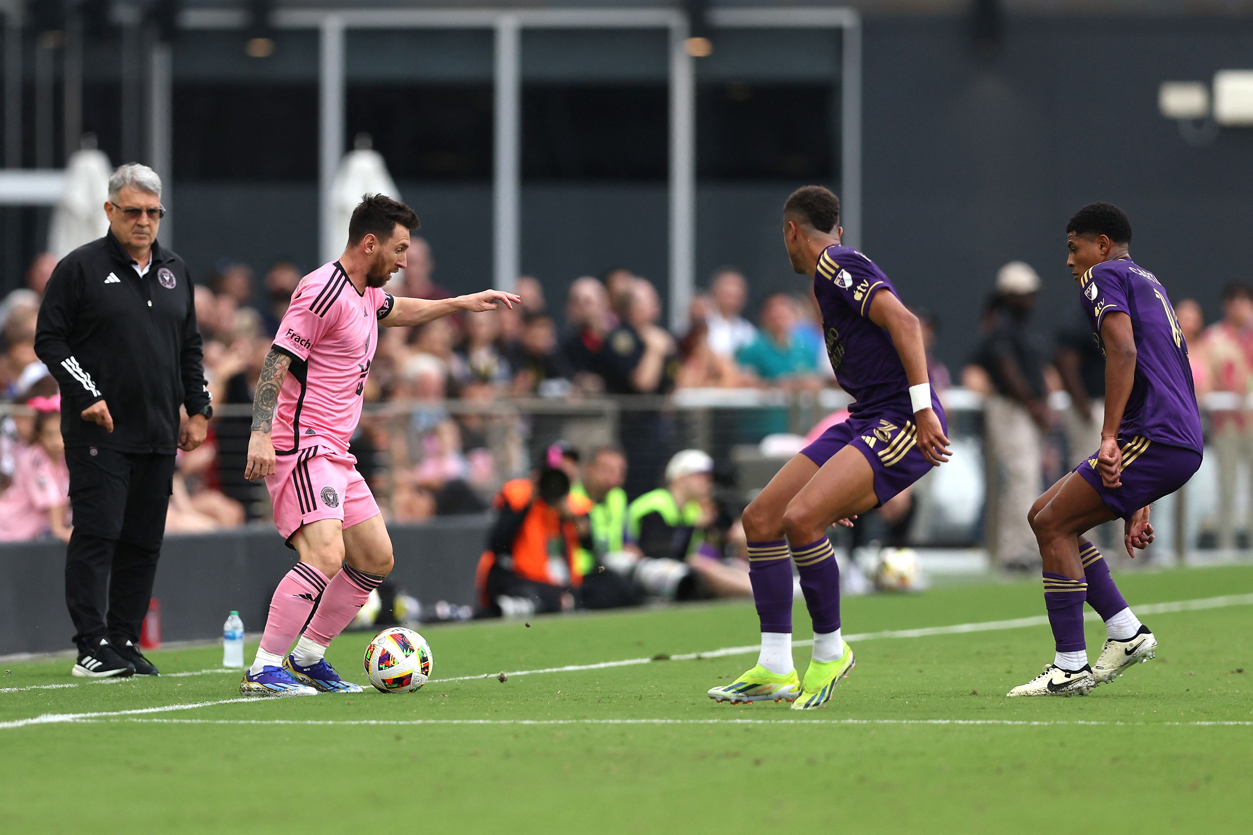 El capitán del Inter Miami, Lionel Messi, se enfrenta a Rafael Santos del Orlando City SC mientras su entrenador, Gerardo Martino, observa la acción en el DRV PNK Stadium.  (Foto Prensa Libre: AFP)