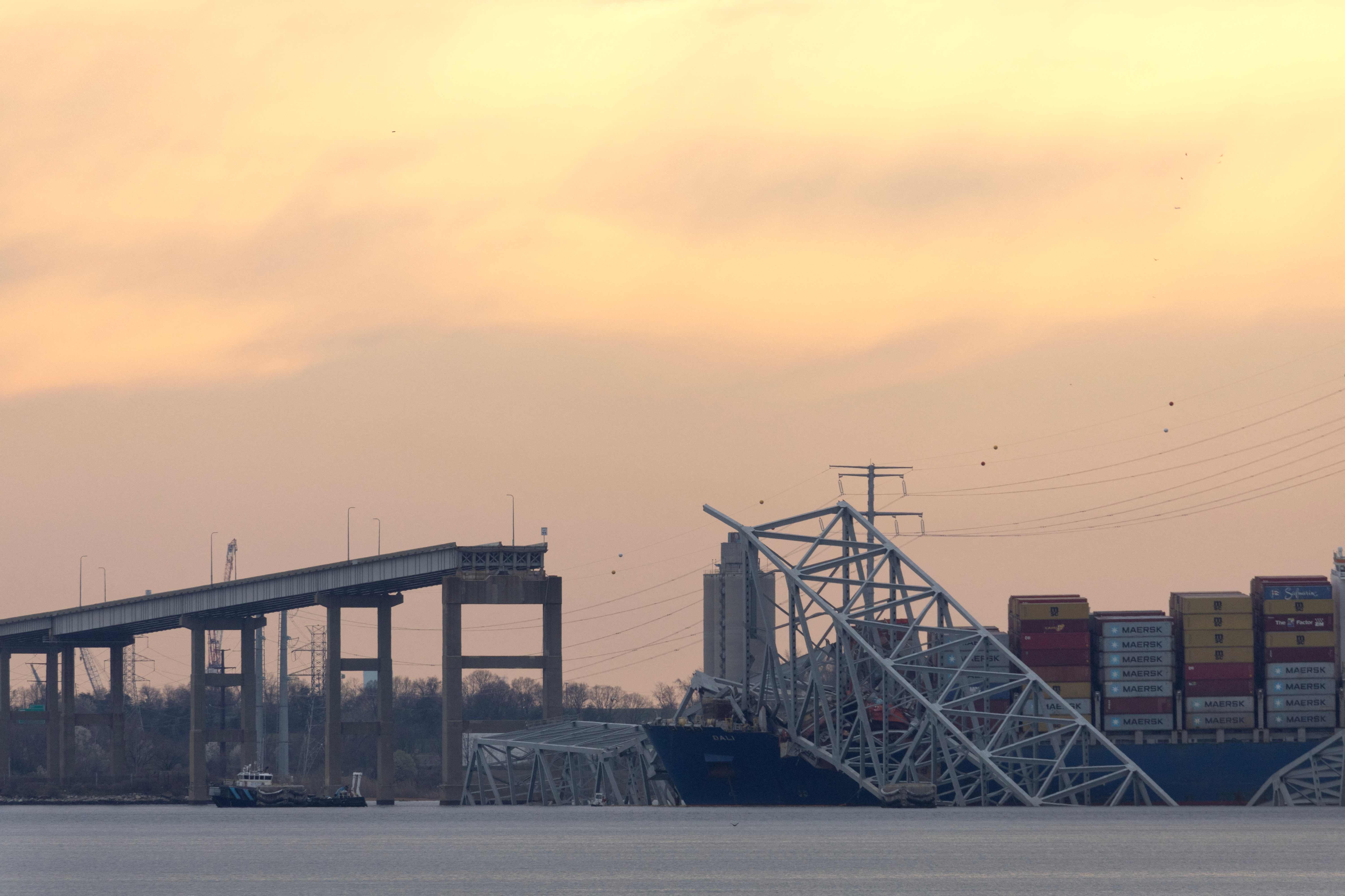 BALTIMORE, MARYLAND - MARCH 28: The sun descends beyond the collapsed Francis Scott Key Bridge on March 28, 2024 in Baltimore, Maryland. The bridge, used by roughly 30,000 vehicles each day, fell into the Patapsco River after being struck by the Dali, a cargo ship leaving the Port of Baltimore at around 1:30 a.m. Tuesday morning. The bodies of two men who were on the bridge at the time of the accident have been recovered from the water, with four others still missing and presumed dead and two others rescued and treated for injuries shortly after the accident. The Port of Baltimore, one of the largest and busiest on the East Coast of the U.S., is temporarily closed.   Scott Olson/Getty Images/AFP (Photo by SCOTT OLSON / GETTY IMAGES NORTH AMERICA / Getty Images via AFP)