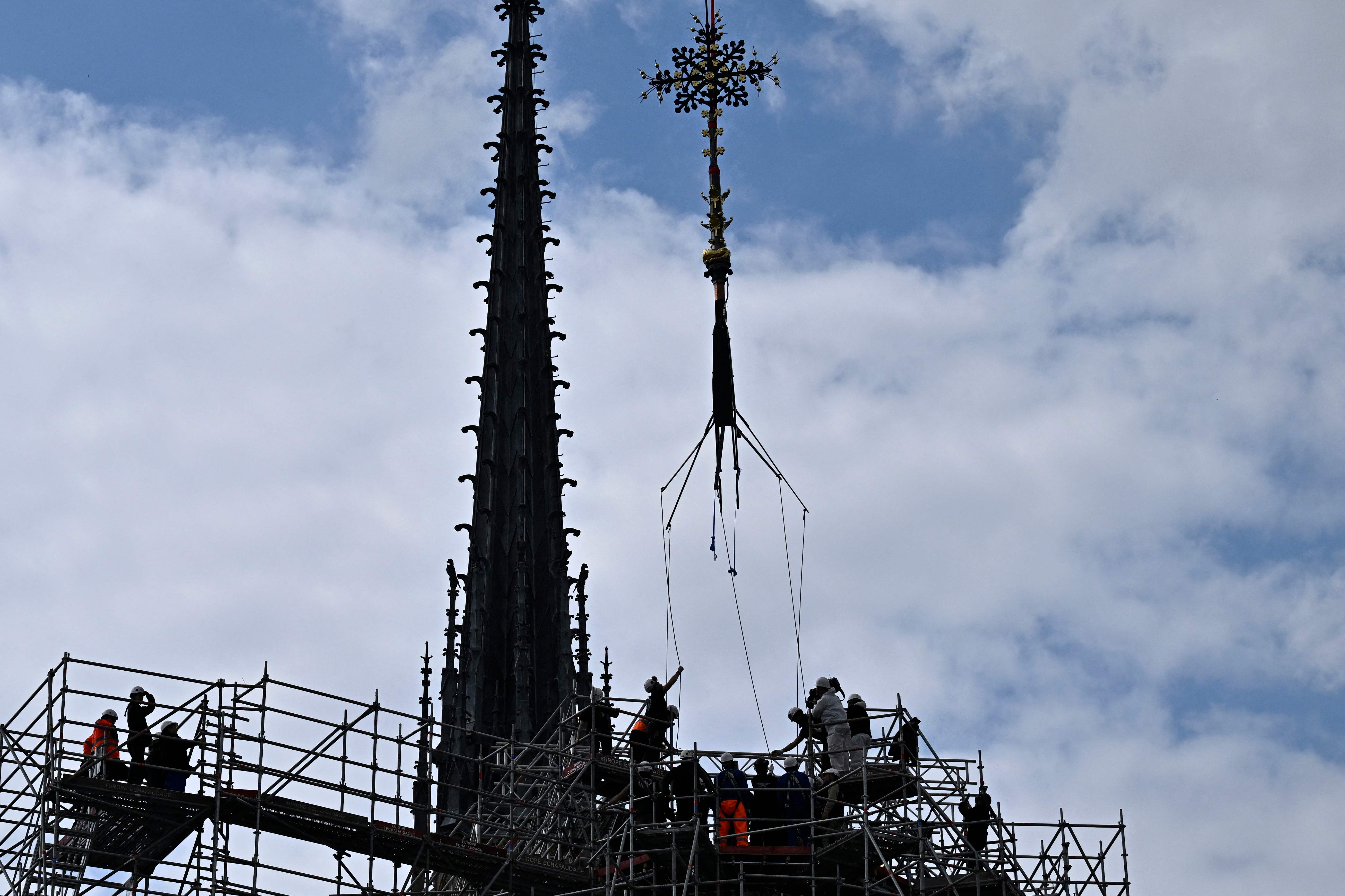 Workers put back in place the cross of the apse of the Notre-Dame de Paris cathedral, in Paris on May 24, 2024. (Photo by JULIEN DE ROSA / AFP)