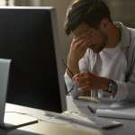 Tired businessman having a headache while working on a computer in the office.