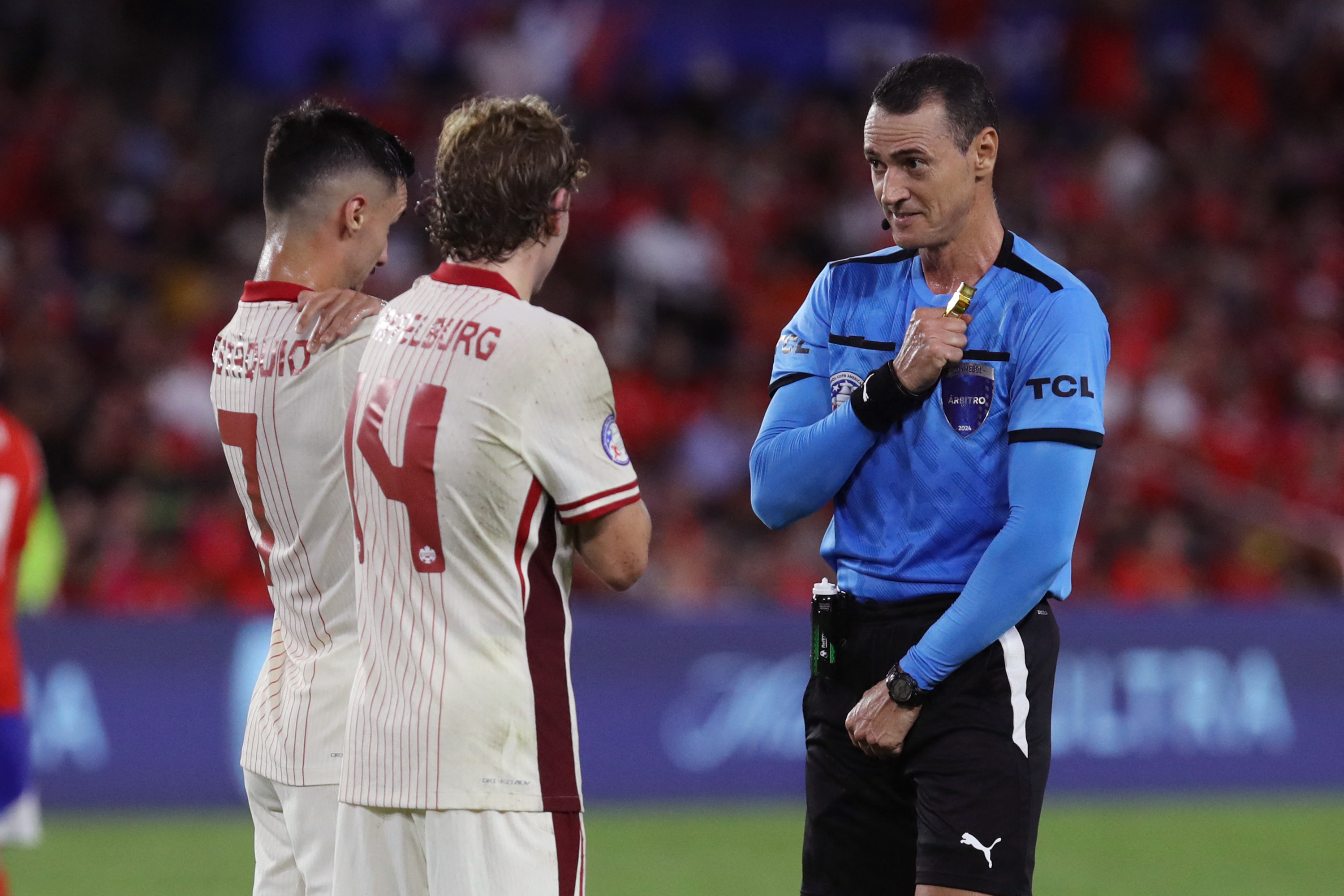 El árbitro, Jesús Valenzuela, habla con Stephen Eustaquio y Jacob Shaffelburg, de Canadá, durante el último partido del Grupo A en la Copa América 2024. (Foto Prensa Libre: AFP)