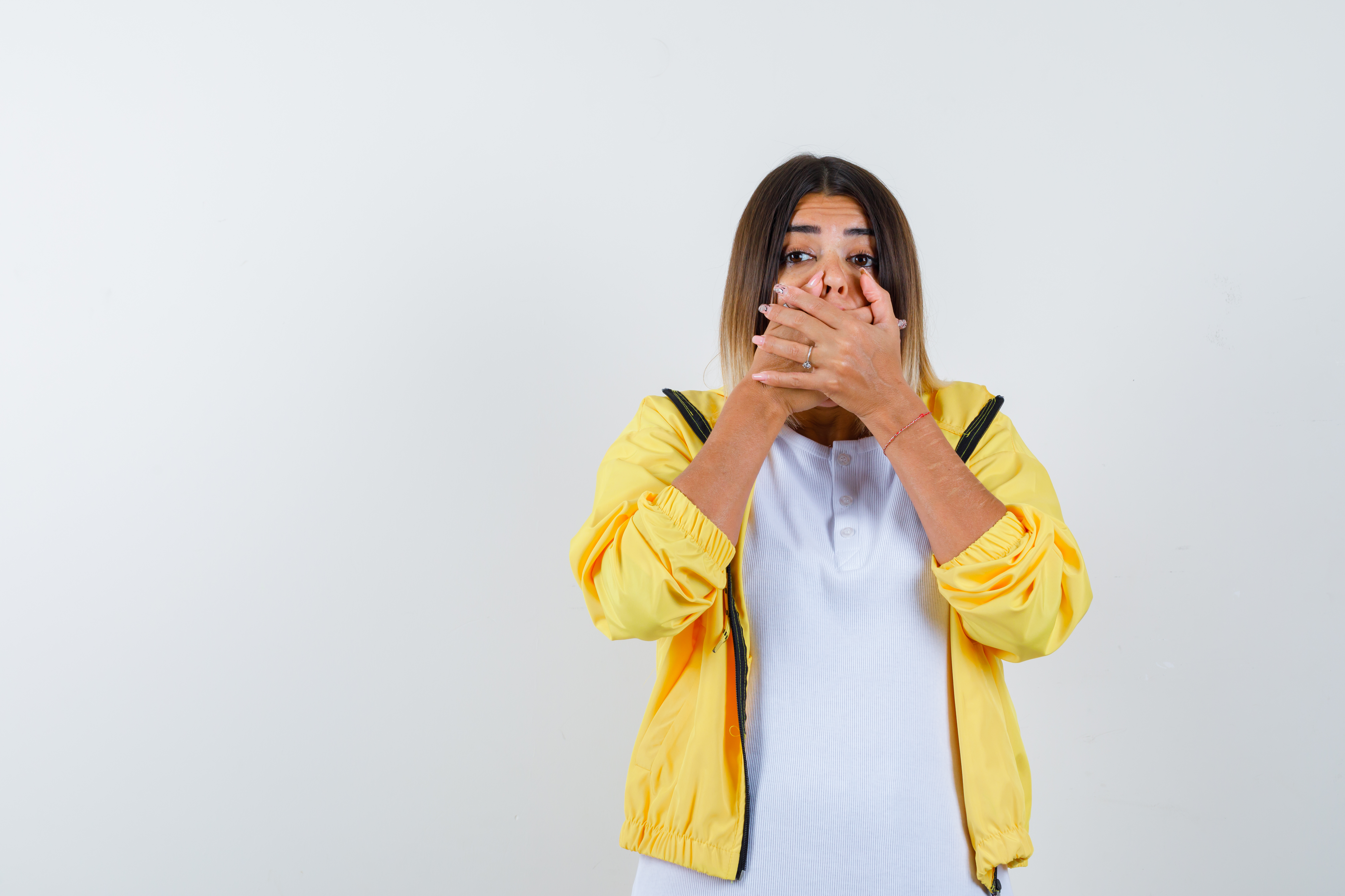 female in t-shirt, jacket keeping hands on mouth and looking scared , front view.