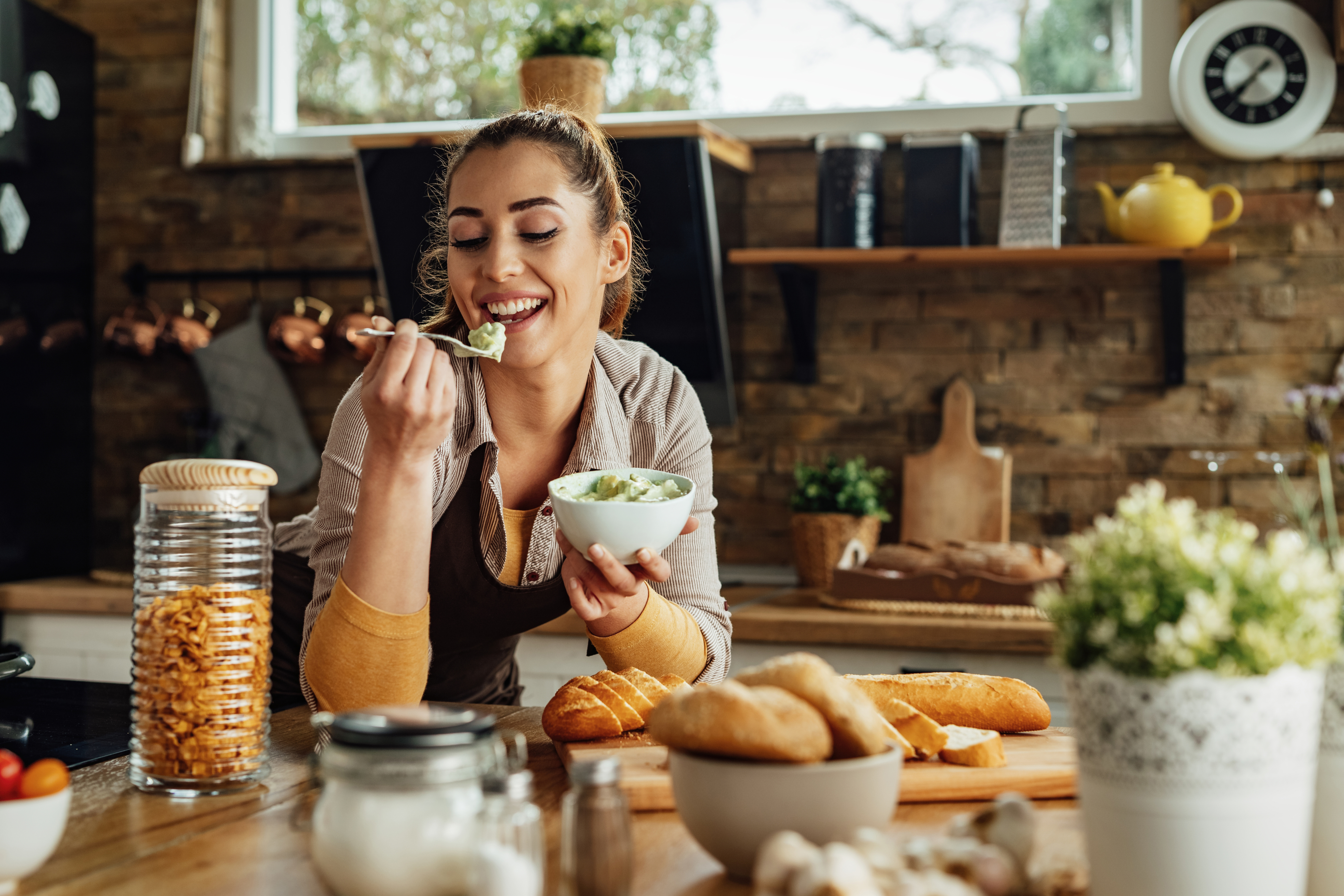 Young happy woman making healthy meal and tasting food in the kitchen.