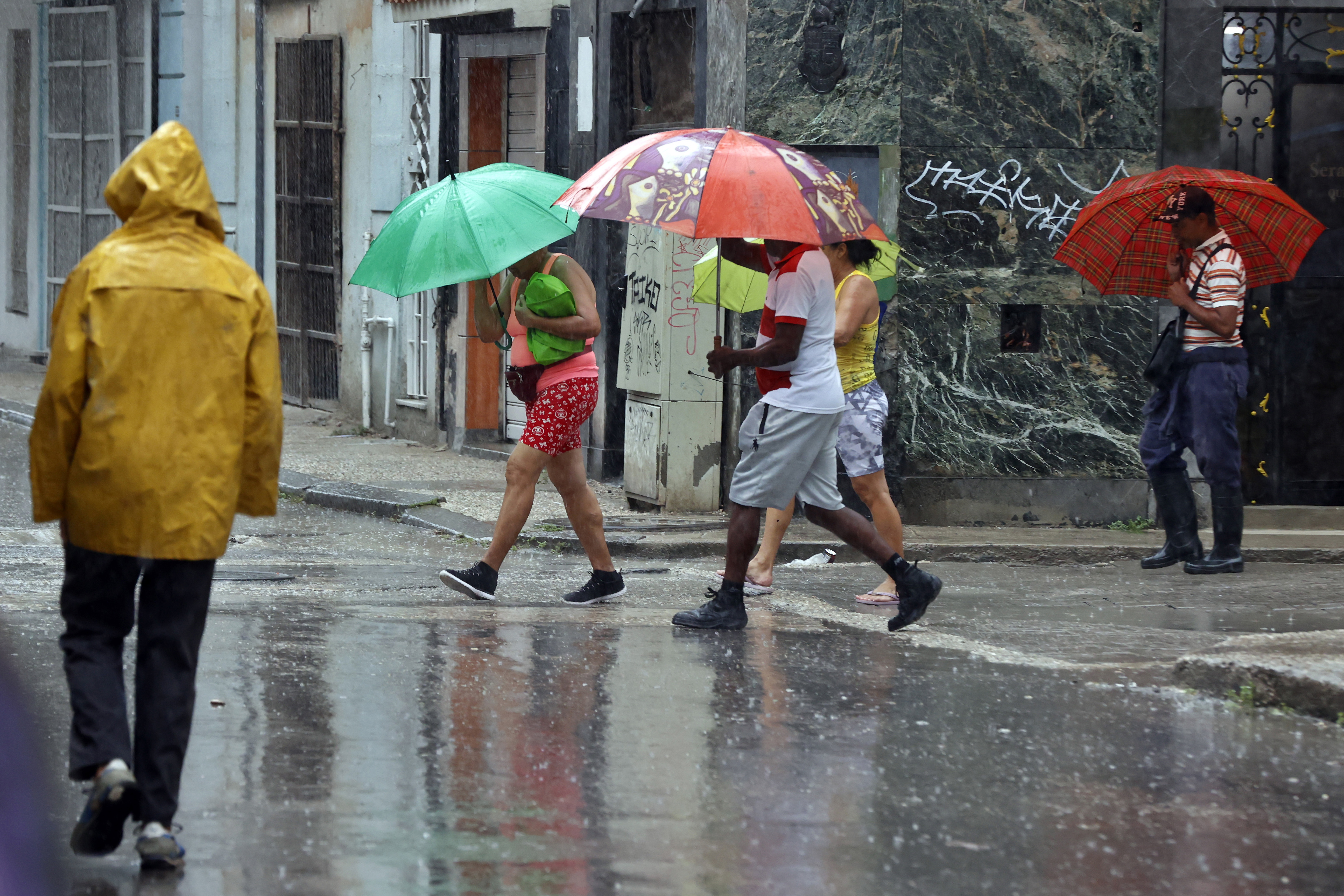 AME2452. LA HABANA (CUBA), 25/09/2024.- Varias personas caminan bajo la lluvia este miércoles en La Habana (Cuba). El oeste de Cuba recibe este miércoles los efectos del huracán Helene con fuertes lluvias y rachas de viento persistentes desde la noche anterior en todo el occidente del país, donde se han adoptado medidas de protección civil y se han movilizado brigadas médicas para atender a las zonas proclives a inundaciones. EFE/ Ernesto Mastrascusa