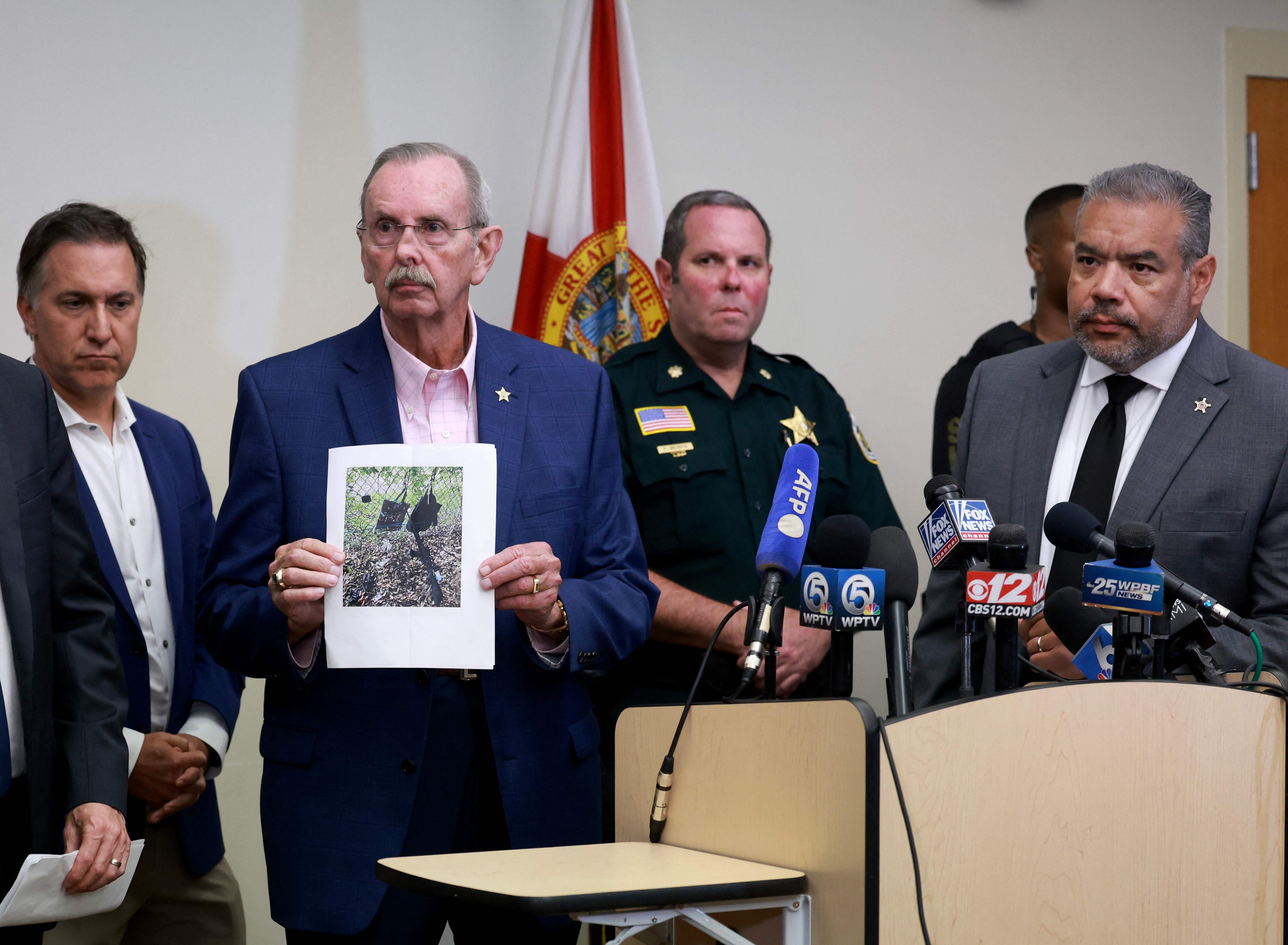 WEST PALM BEACH, FLORIDA - SEPTEMBER 15: Palm Beach County Sheriff Ric Bradshaw, holds a photograph of the rifle and other items found near where a suspect was discovered as he stands with Rafael Barros (R), special agent in charge of the US Secret Service's Miami field office during a press conference regarding an apparent assassination attempt of former President Donald Trump on September 15, 2024 in West Palm Beach, Florida. The FBI and U.S. Secret Service, along with the Palm Beach County Sheriff's office, are investigating the incident, which the FBI said "appears to be an attempted assassination of former President Trump' while he was golfing at Trump International Golf Club.   Joe Raedle/Getty Images/AFP (Photo by JOE RAEDLE / GETTY IMAGES NORTH AMERICA / Getty Images via AFP)