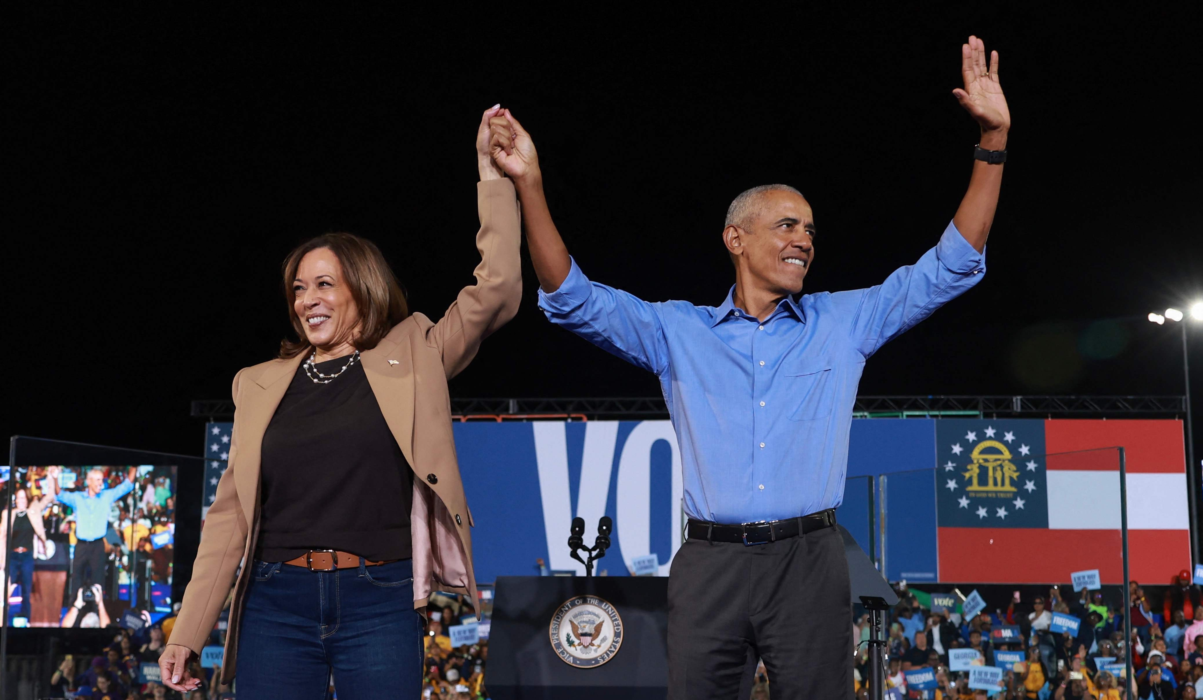 El expresidente estadounidense Barack Obama (d) conversa con la candidata presidencial del partido demócrata Kamala Harris (i) durante un acto electoral celebrado en el estadio James R. Hallford de Clarkston, Georgia, Estados Unidos.