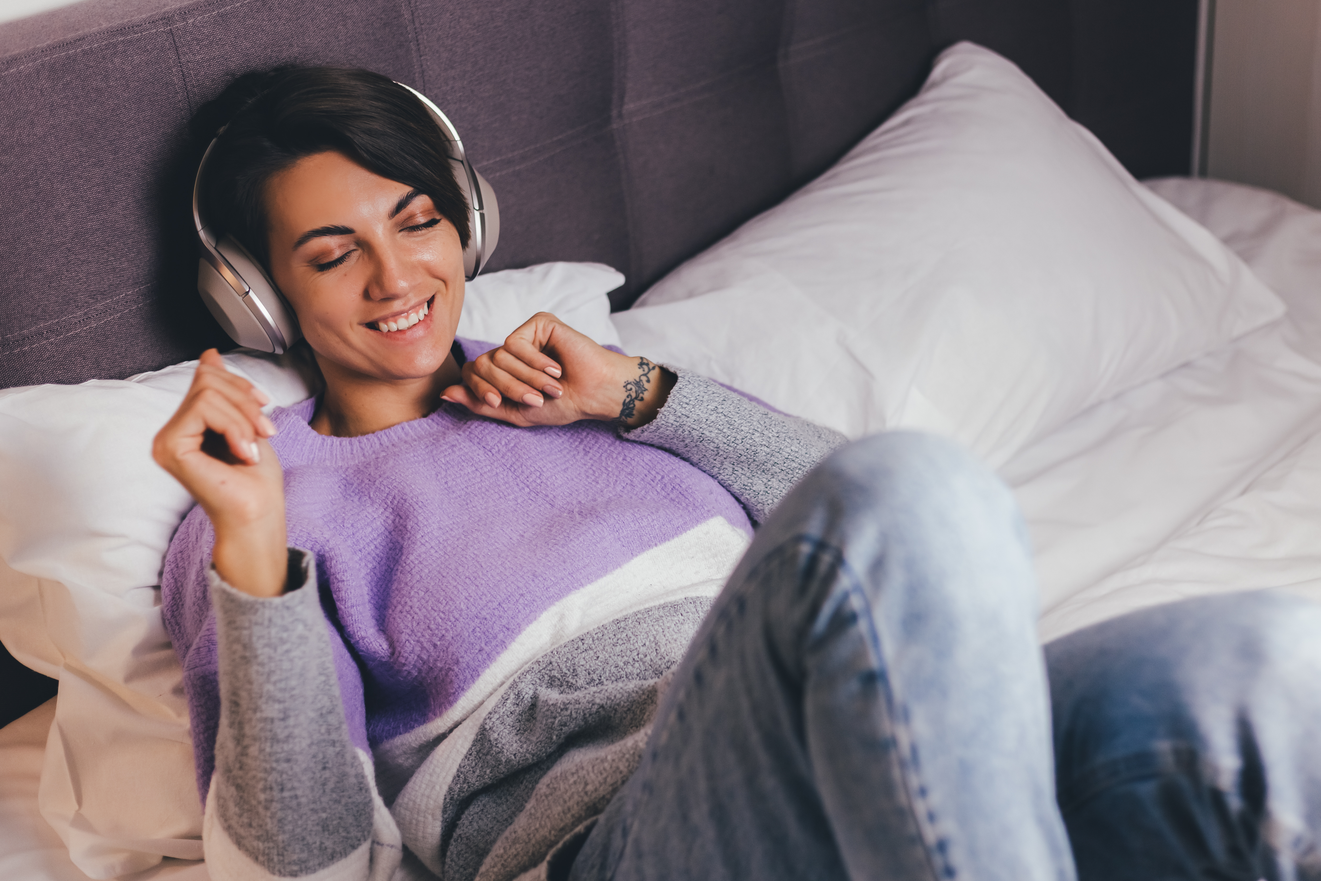 Mujer feliz en casa en una cama cómoda vistiendo un jersey de ropa abrigada, escuchando música