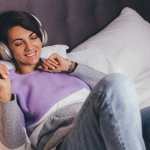 Mujer feliz en casa en una cama cómoda vistiendo un jersey de ropa abrigada, escuchando música