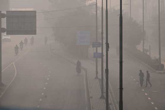 Commuters move along a street engulfed in thick smog in Lahore on November 22, 2024. (Photo by Arif ALI / AFP)